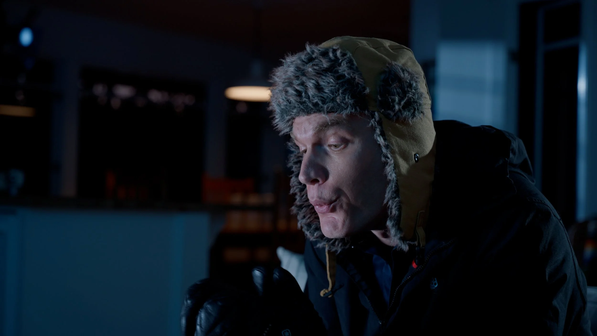 Person wearing a fur-trimmed winter hat and gloves indoors, dimly lit setting