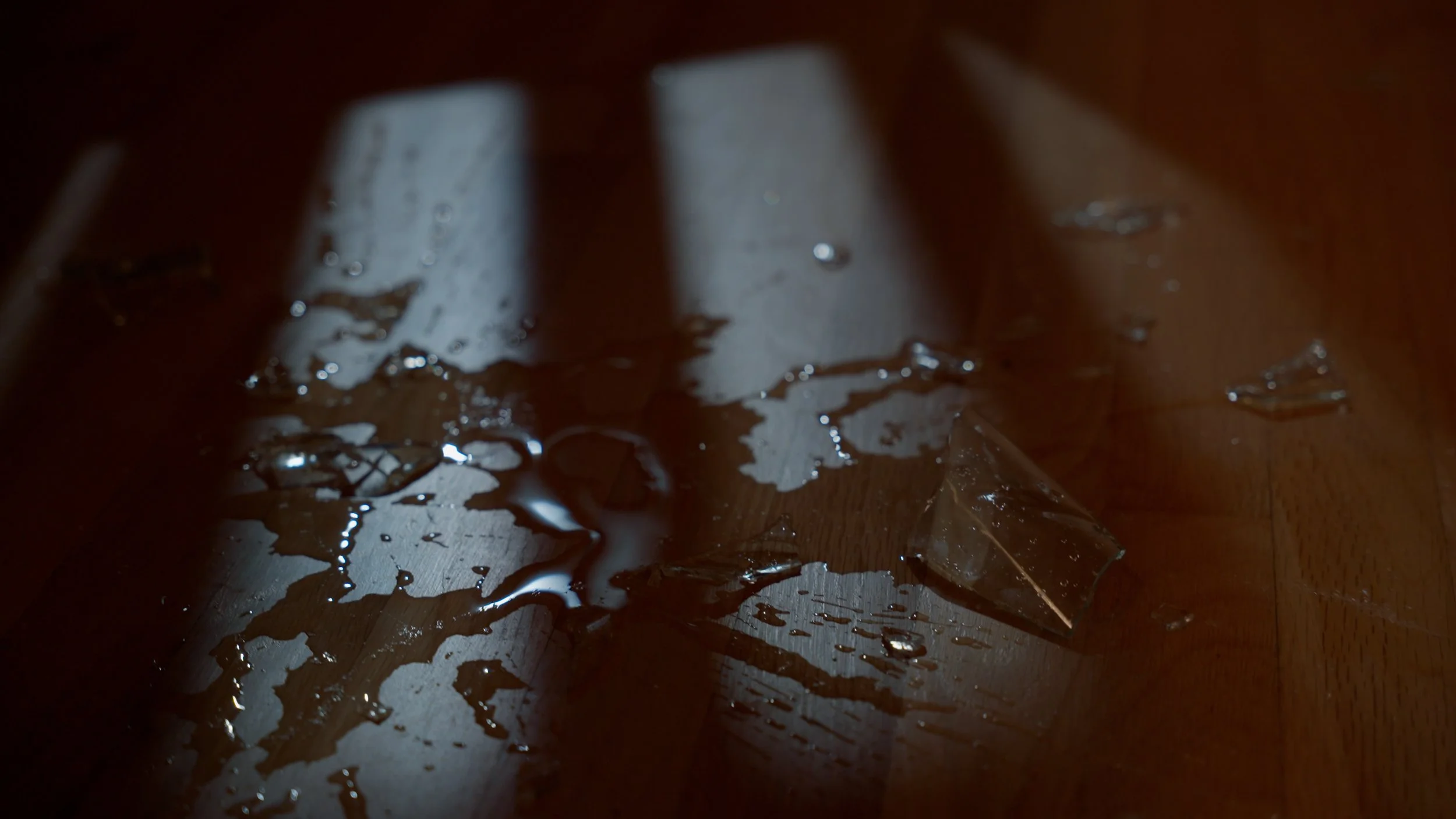 Spilled liquid and glass fragments on wooden floor with shadows