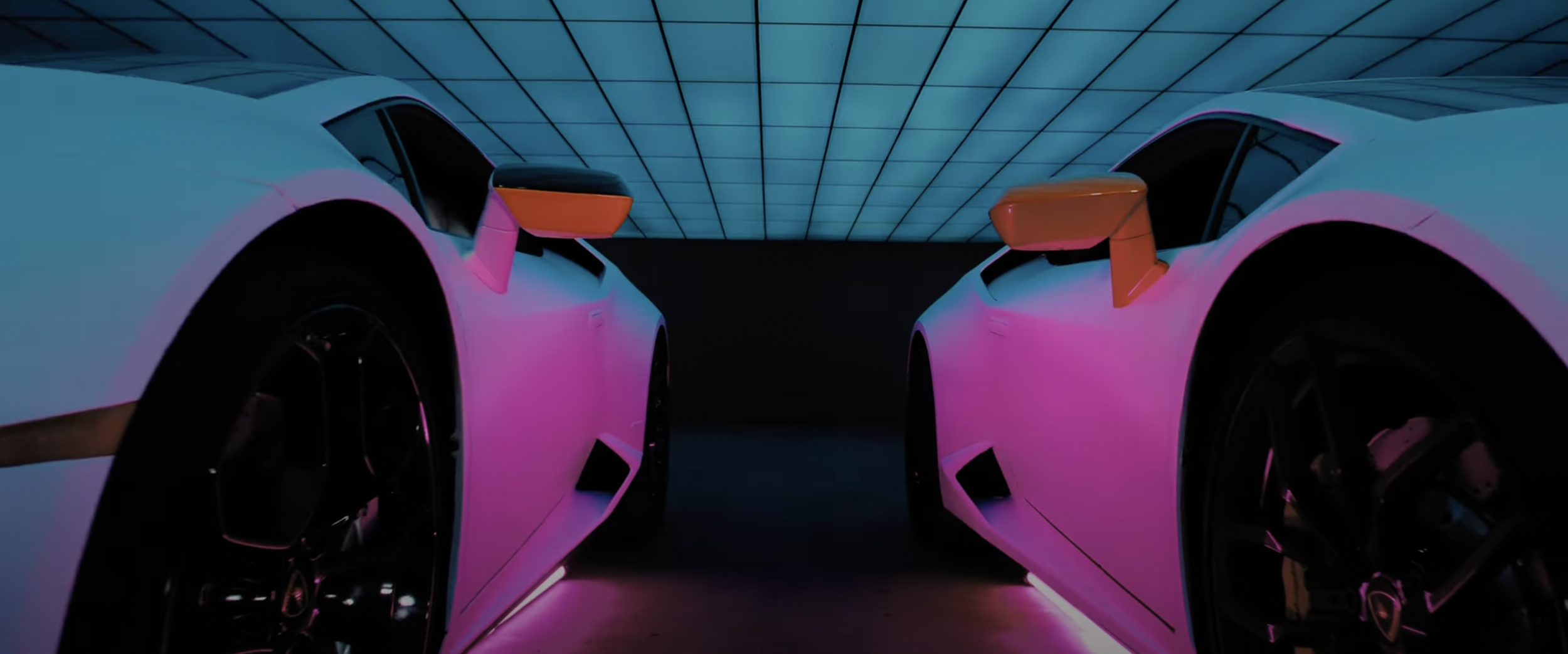Two sports cars facing each other with neon lighting, showing close-up of wheels and side mirrors in a modern garage.