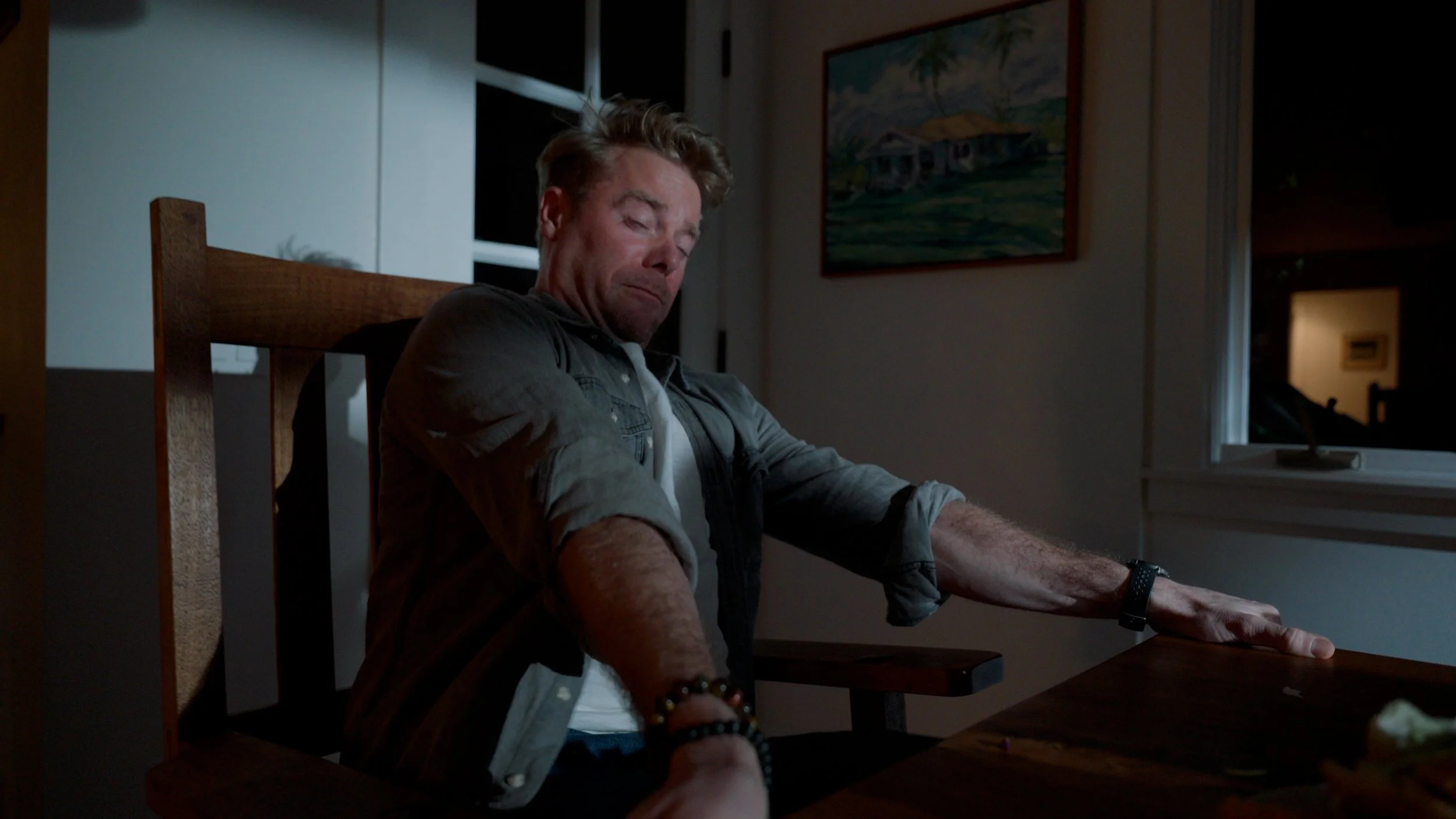 Man sitting at a table with a surprised expression, arms outstretched, indoors.