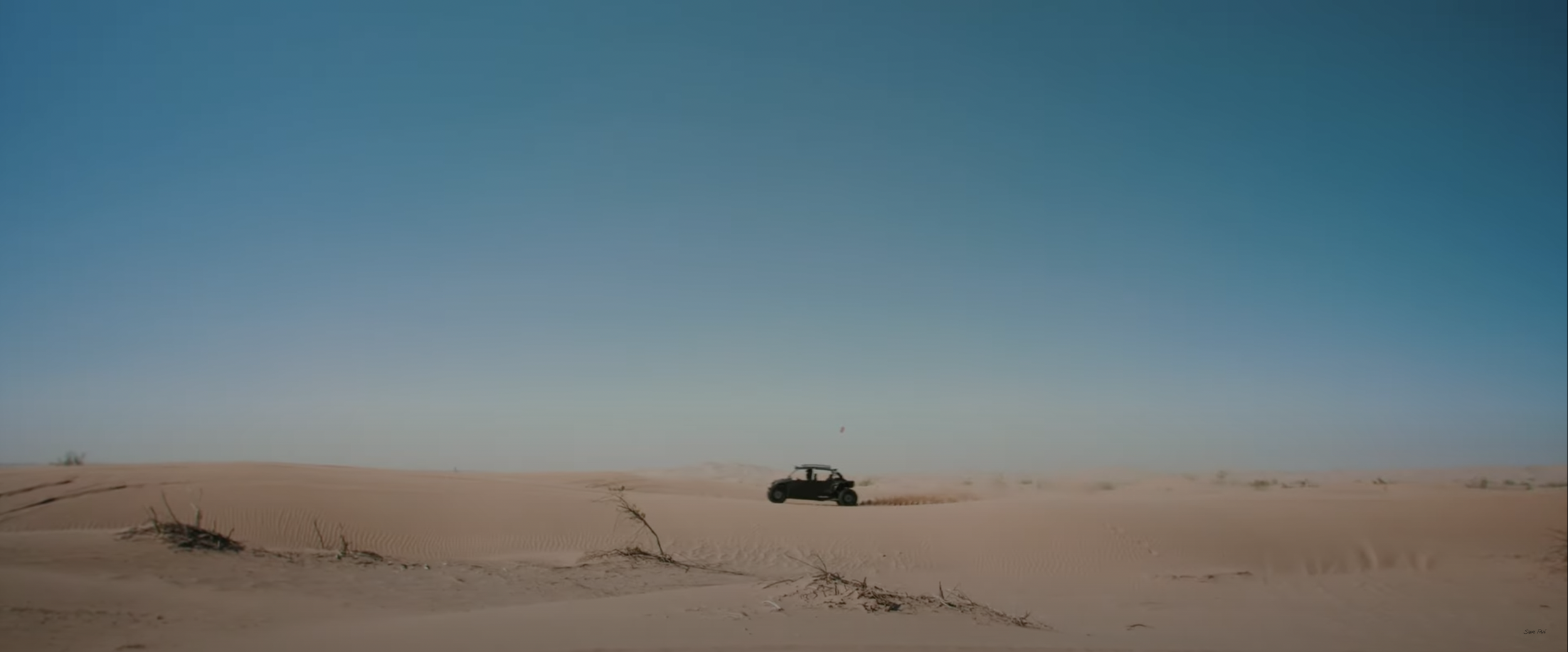 Desert landscape with a dune buggy on sand dunes under a clear blue sky.