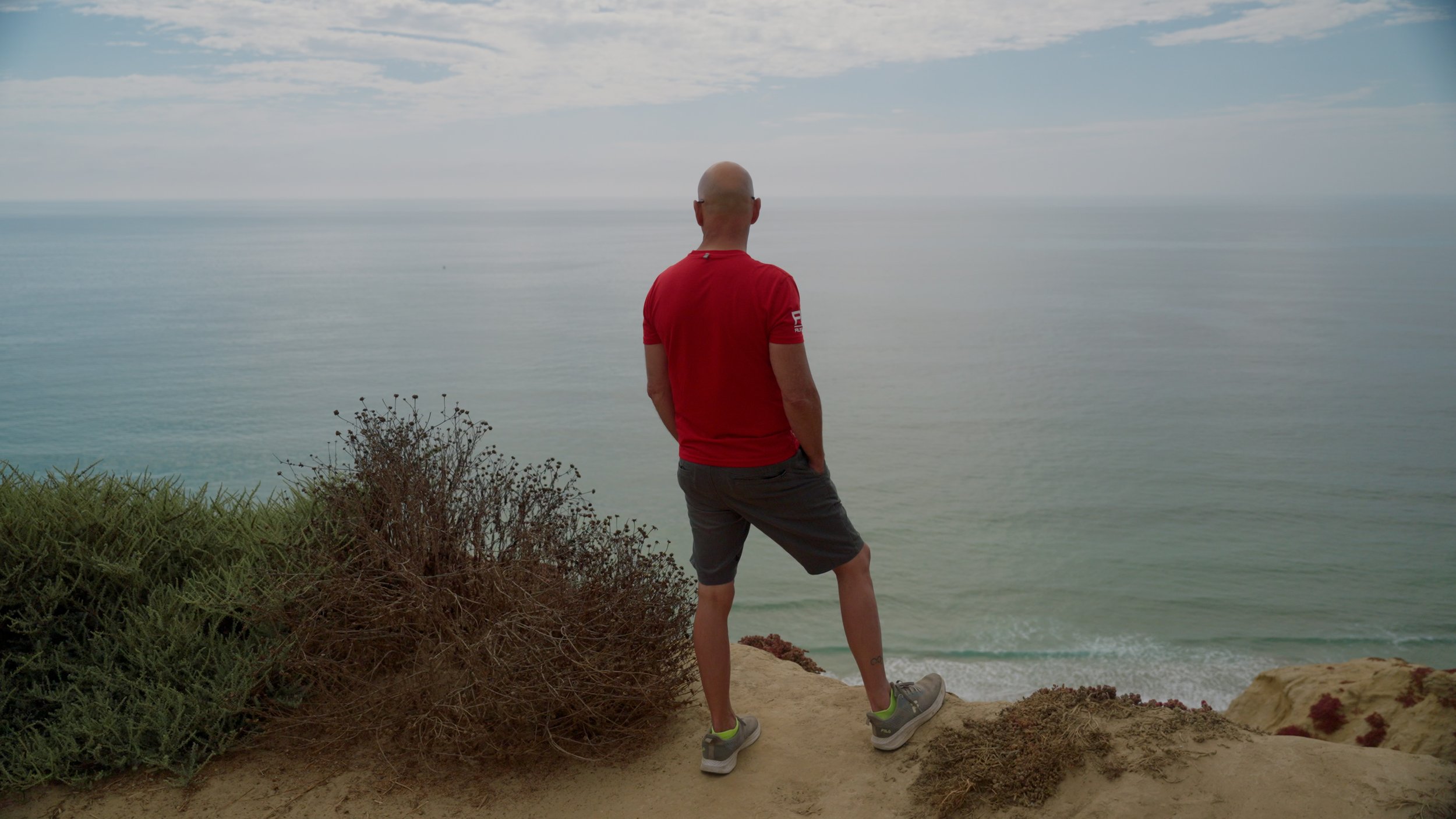 Man in red shirt standing on cliff overlooking ocean