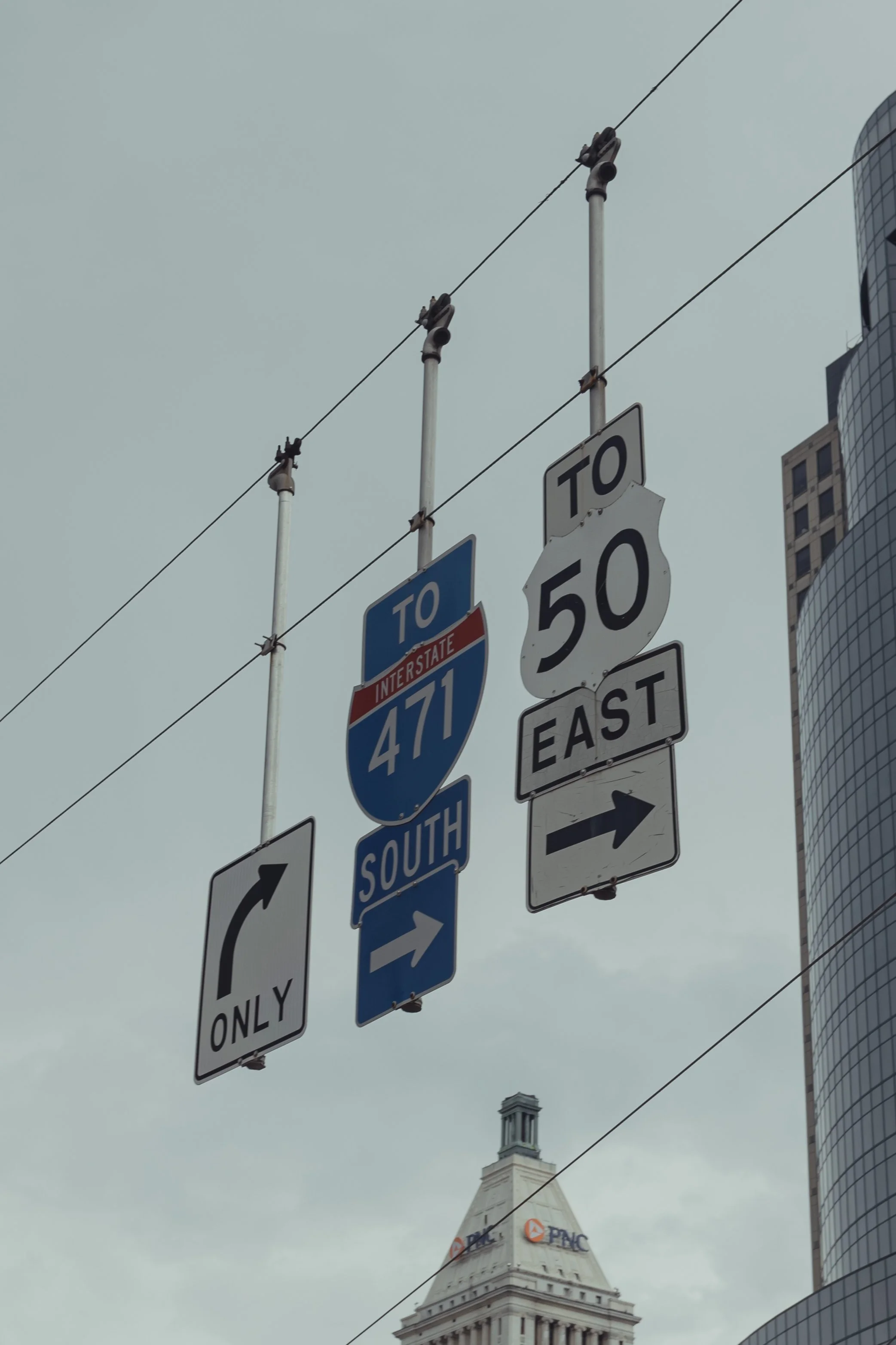 Traffic signs indicating directions to Interstate 471 South and U.S. Route 50 East, with a cloudy sky and tall buildings in the background.