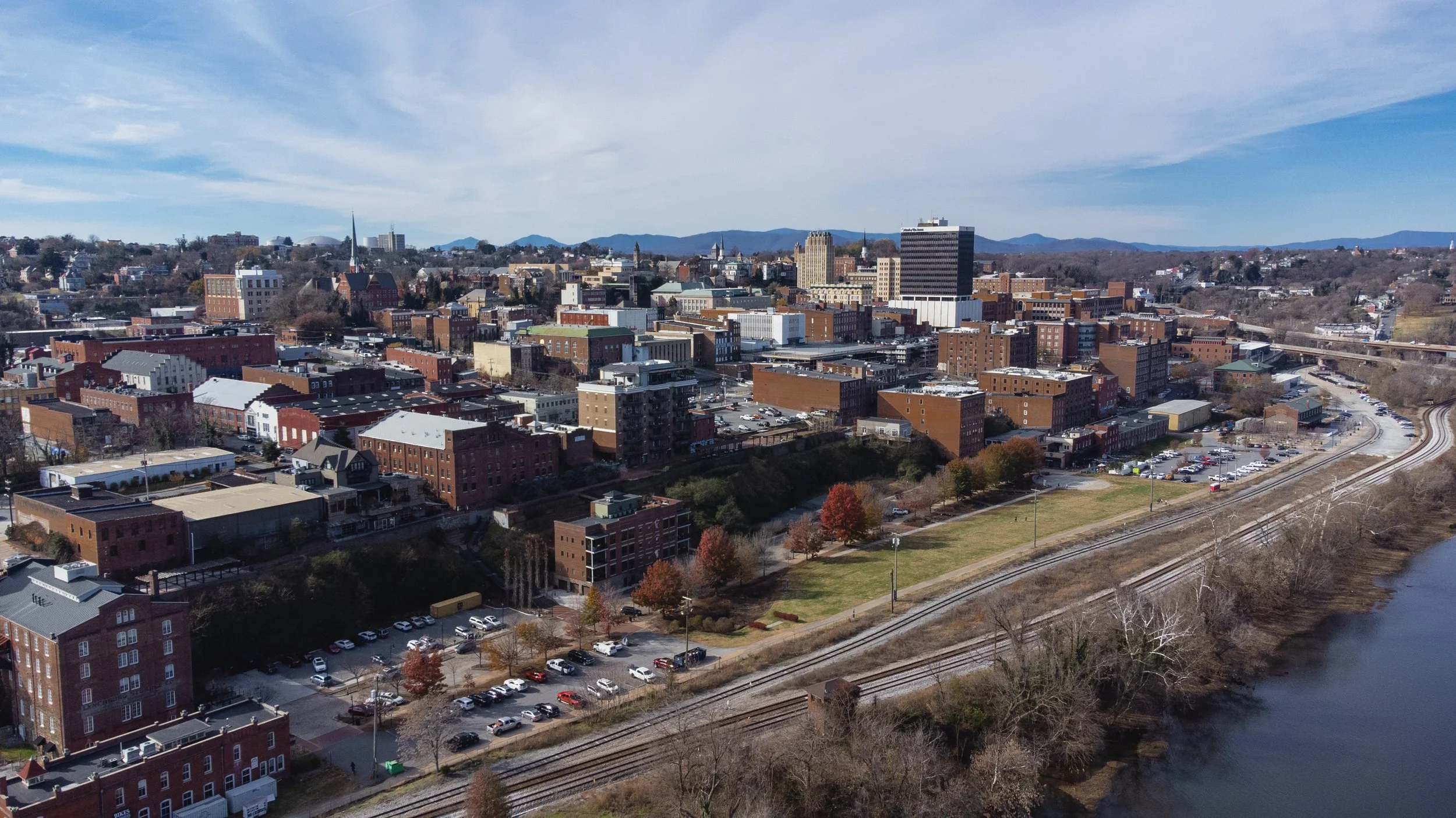 Aerial view of a city with a mix of historic and modern buildings, a river on the right, and train tracks along the riverbank.