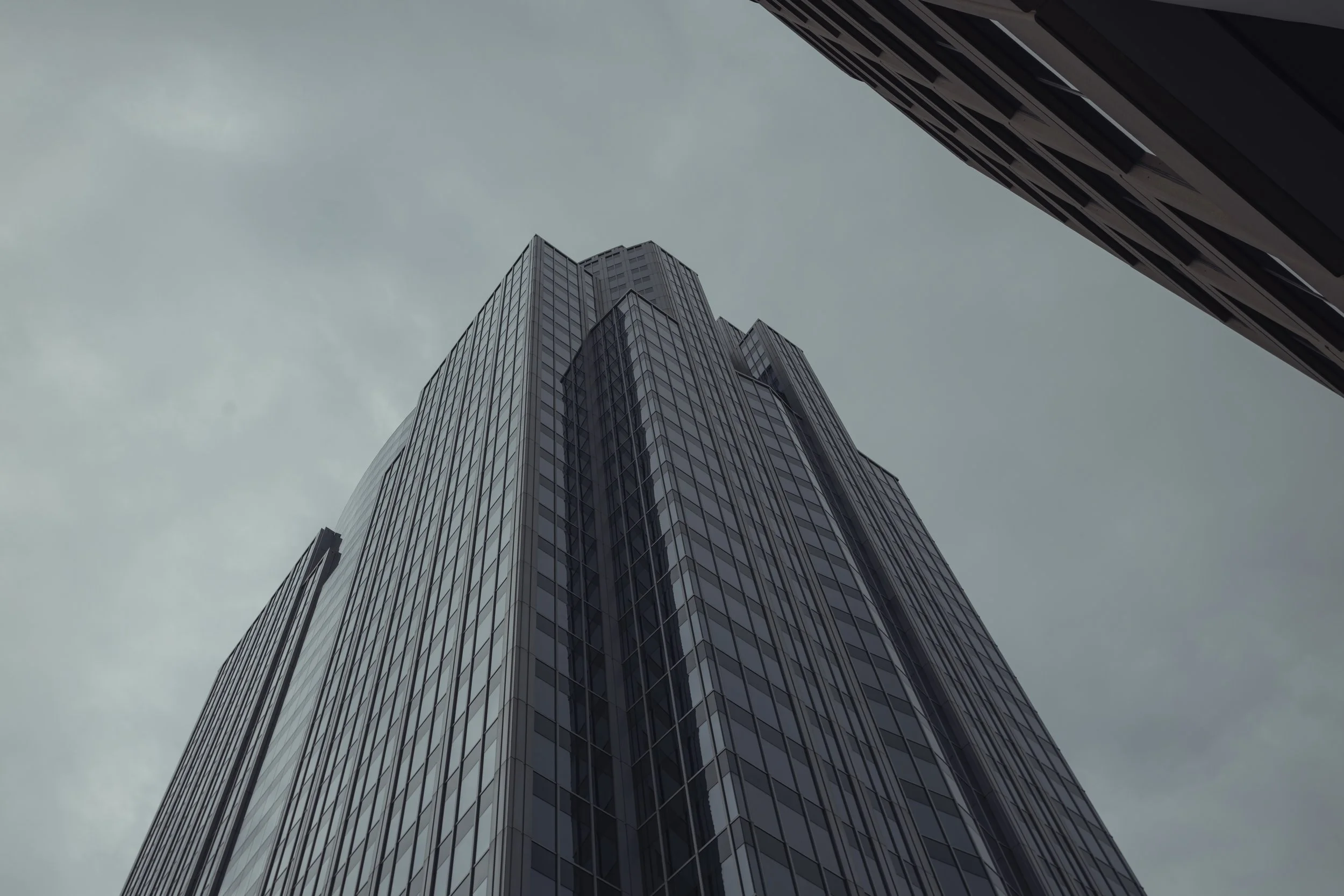 Looking up at a tall, modern skyscraper with reflective glass windows on an overcast day.
