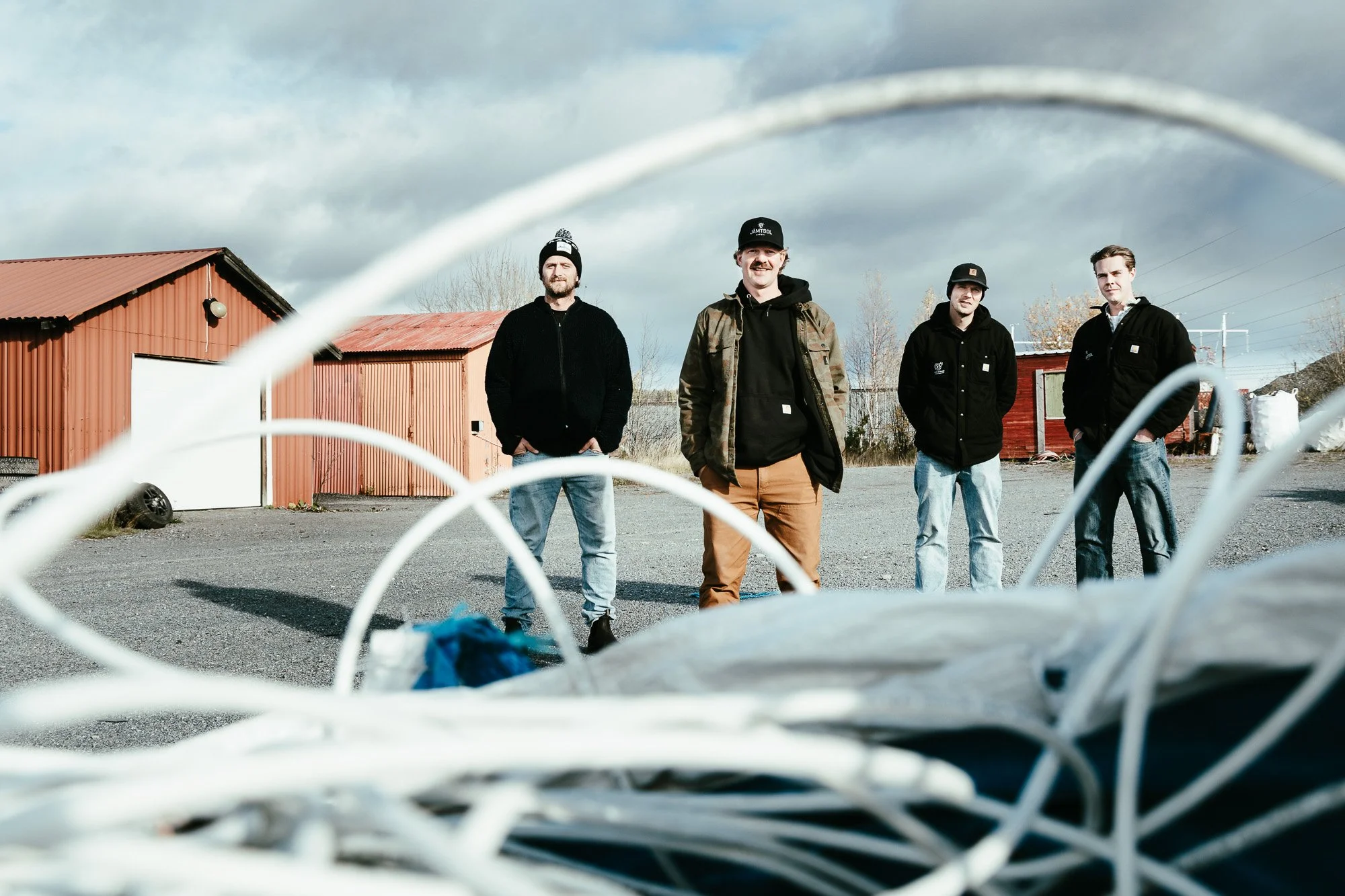 Grundarna till JS El och Metall står på sin tomt i industriområdet Lugnvik i Östersund. Fyra män i arbetsjackor och jeans framför en röd skjulbyggnad.