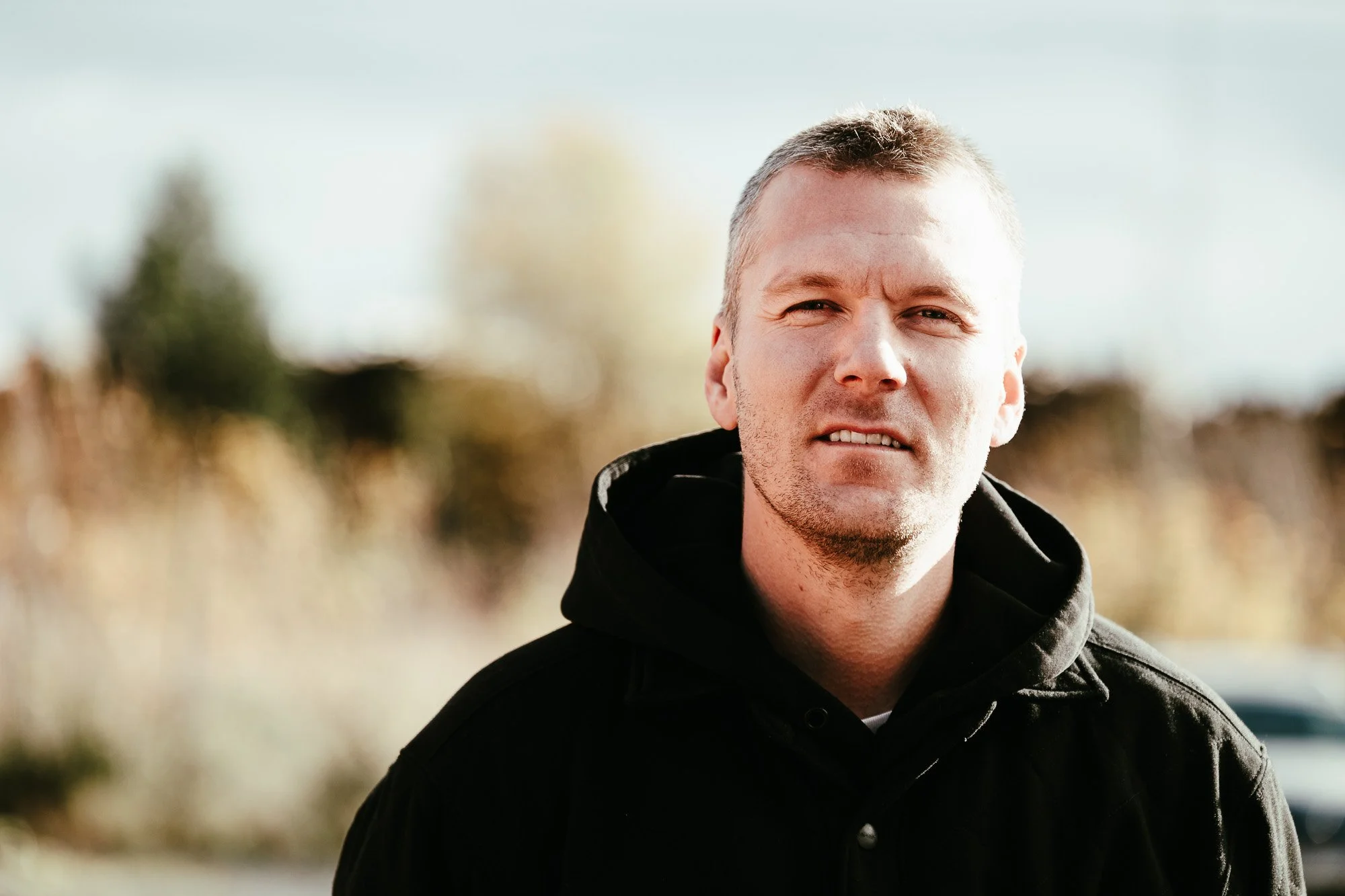 Porträtt av Jocke Danielsson på JS El & Metall. Han bär en svart jacka med huva. I bakgrunden syns suddig natur i höstfärger.