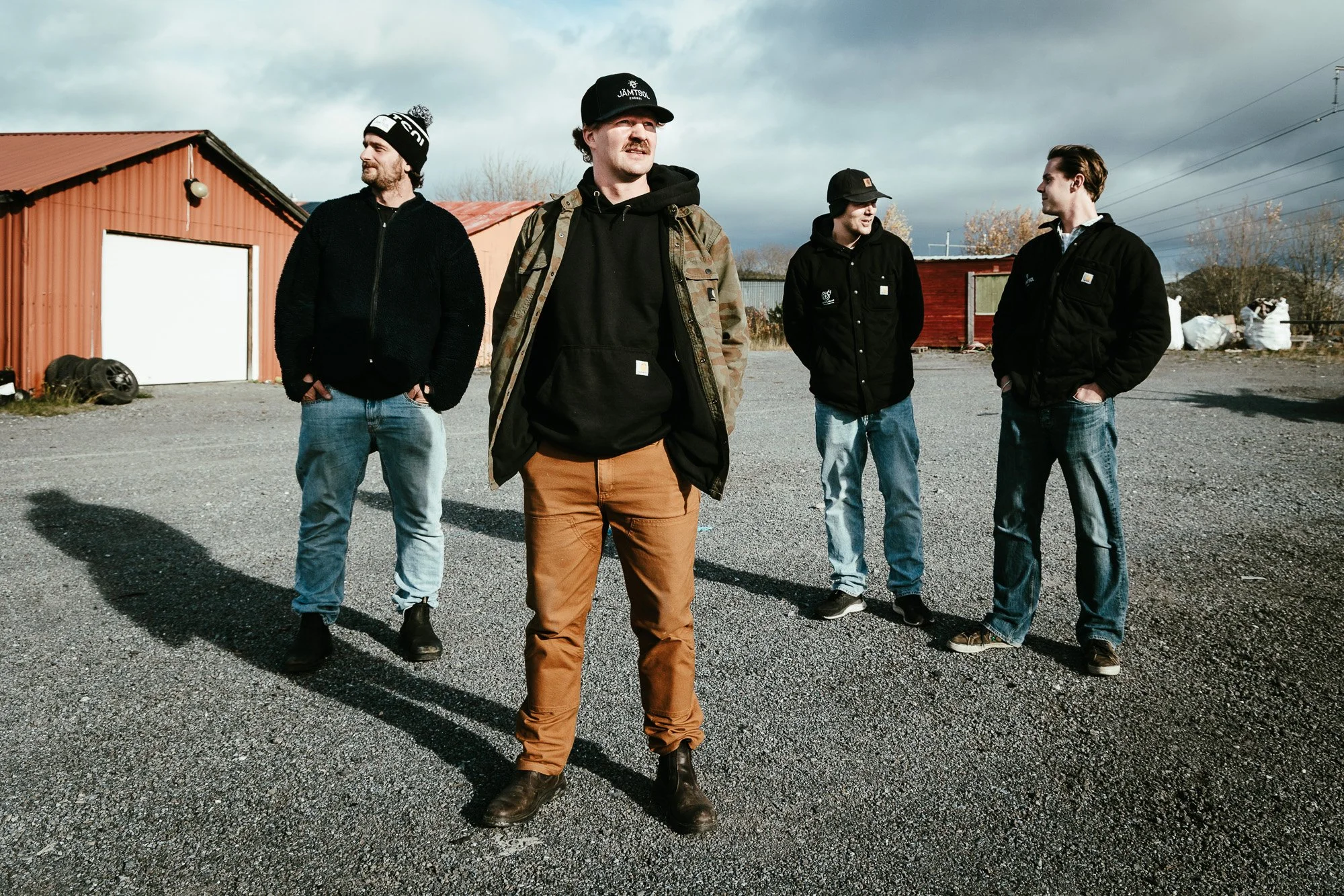 Grundarna till JS El och Metall står på sin tomt i industriområdet Lugnvik i Östersund. Fyra män i arbetsjackor och jeans framför en röd skjulbyggnad.