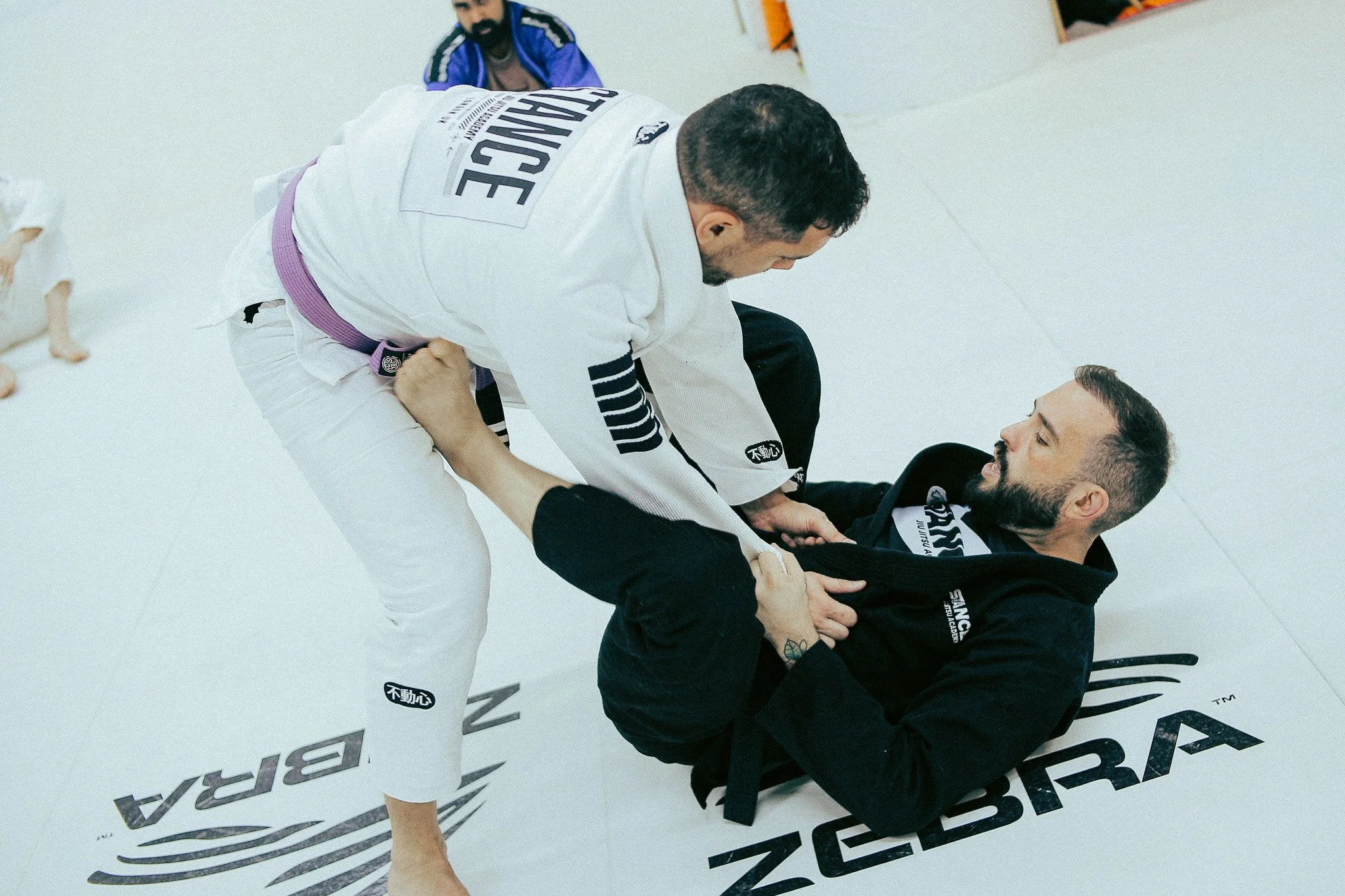 Martial arts instructor in black gi with black belt giving instruction to children in white gis at a martial arts dojo.
