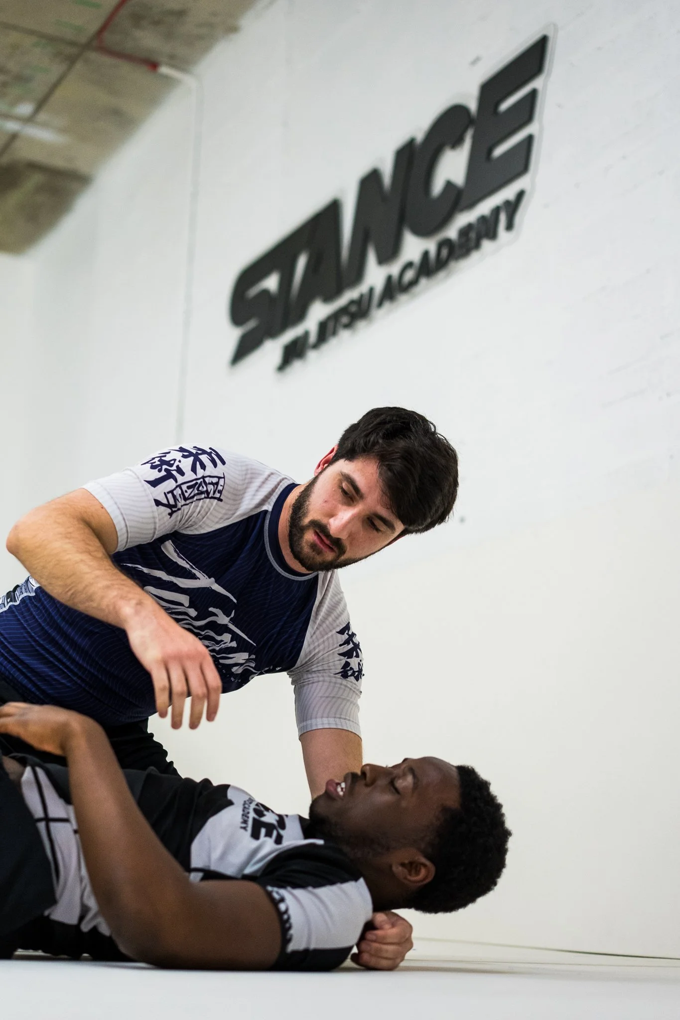 Two men on a martial arts gym mat, with one standing and the other lying down, during a training or sparring session at SianCe Muay Thai Academy.