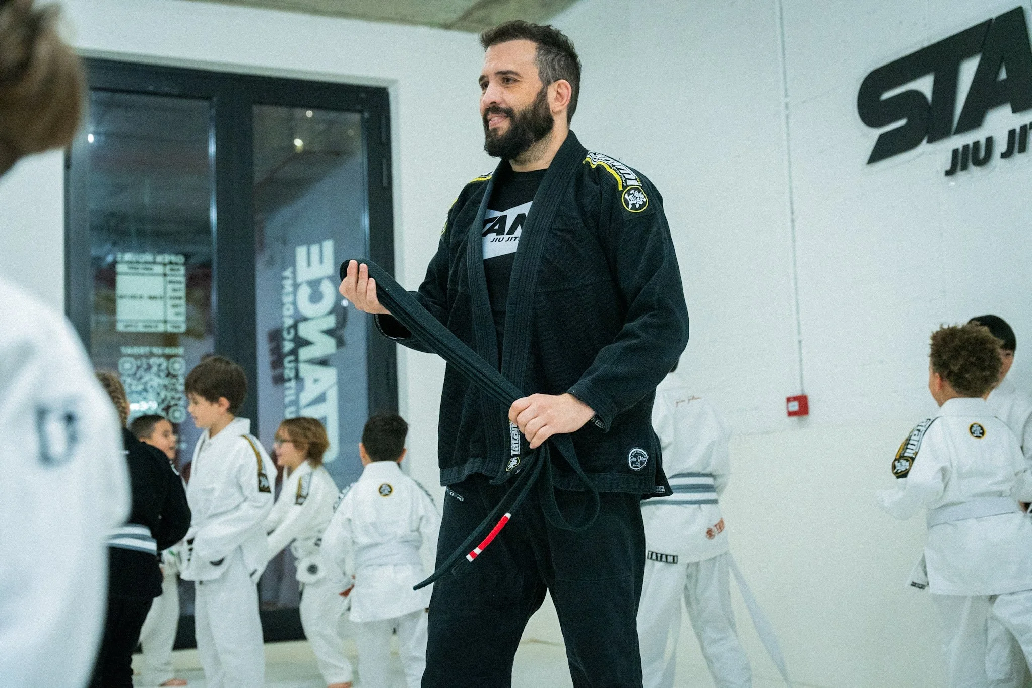 Martial arts instructor in black gi with black belt giving instruction to children in white gis at a martial arts dojo.