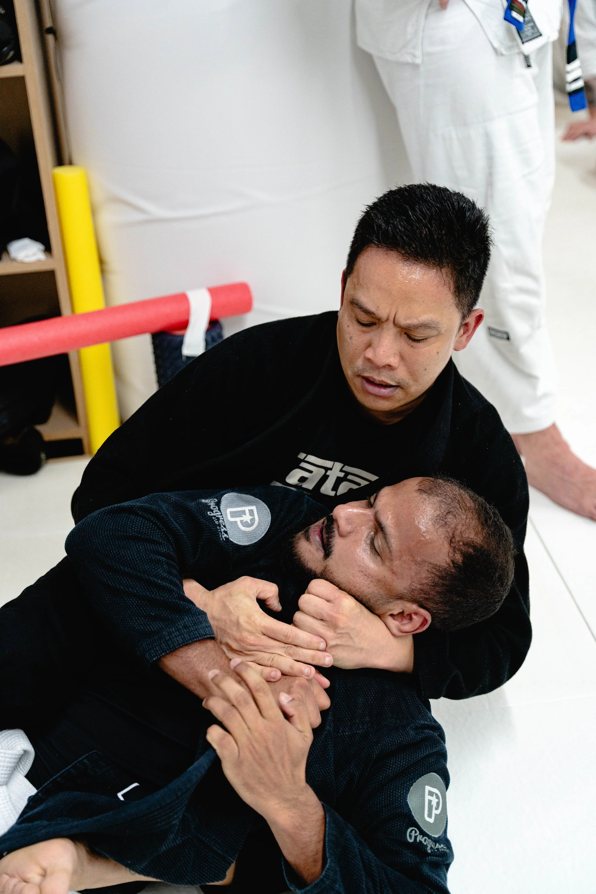 Martial arts instructor in black gi with black belt giving instruction to children in white gis at a martial arts dojo.