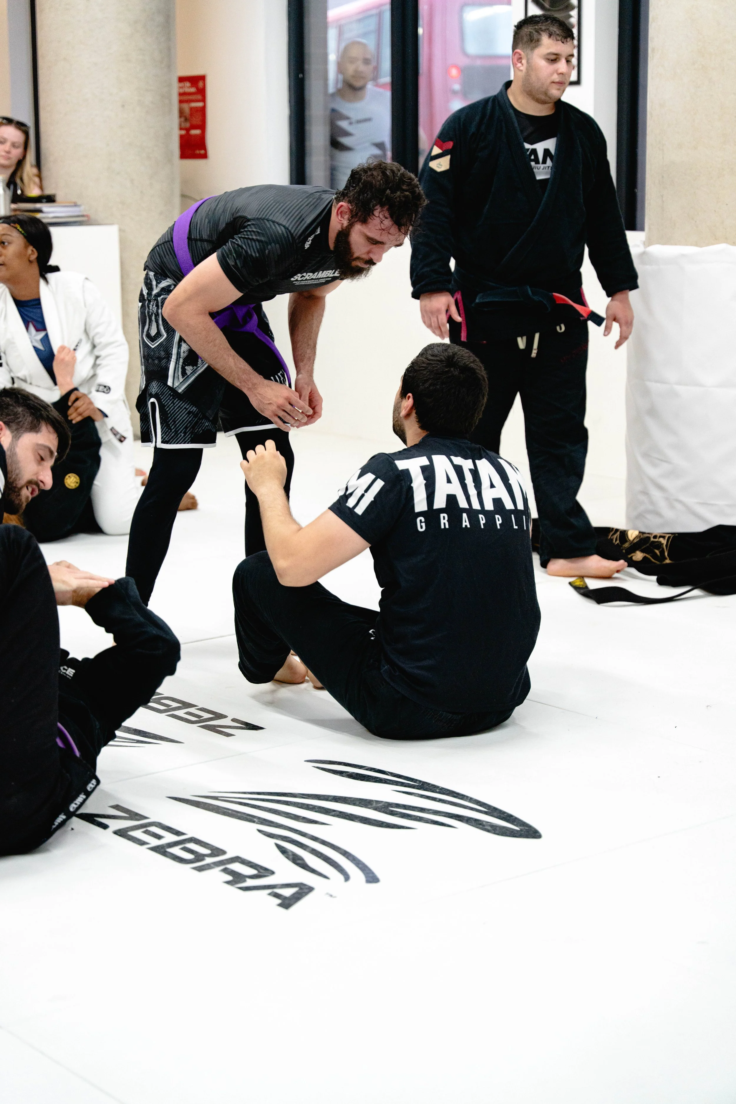 Martial arts instructor in black gi with black belt giving instruction to children in white gis at a martial arts dojo.