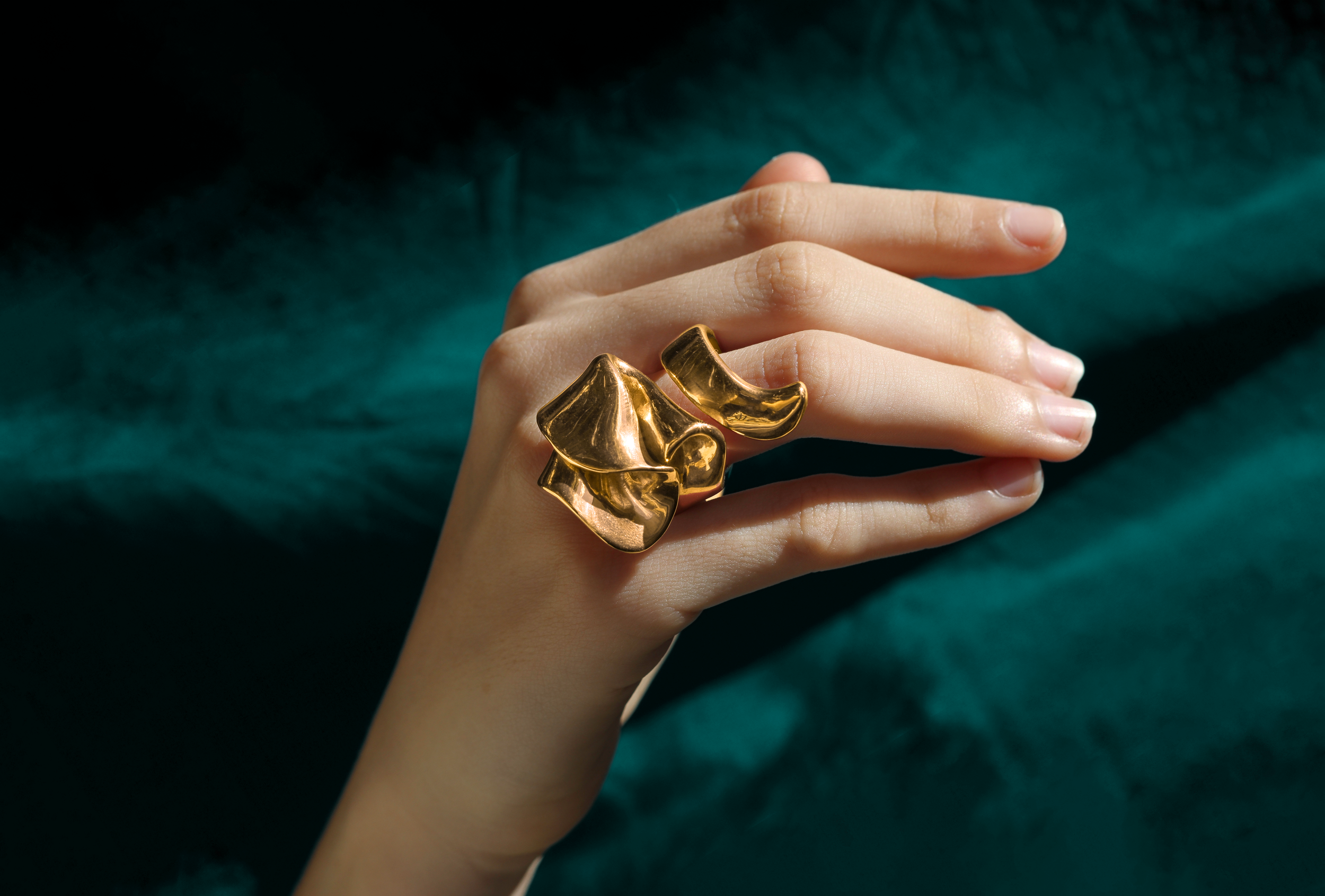 Hand with striking gold ring. Deep teal velvet.