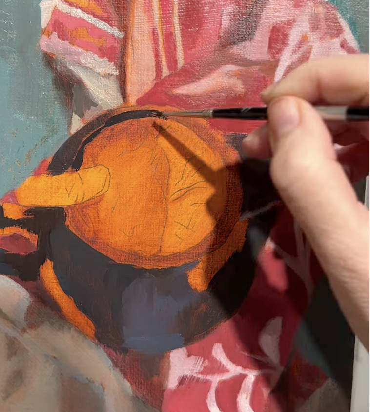 Close-up of an artist's hand painting an orange and black coffee mug on a canvas, with a colorful fabric in the background.