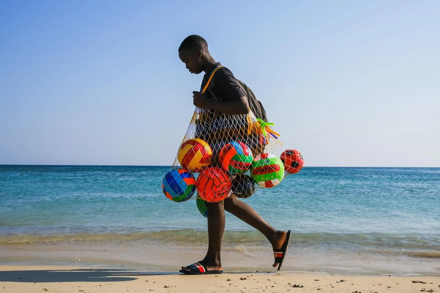 Ballboy. A young street vendor walks the shoreline, selling colorful beach balls to make a living. 
#italiansummer #ferragosto