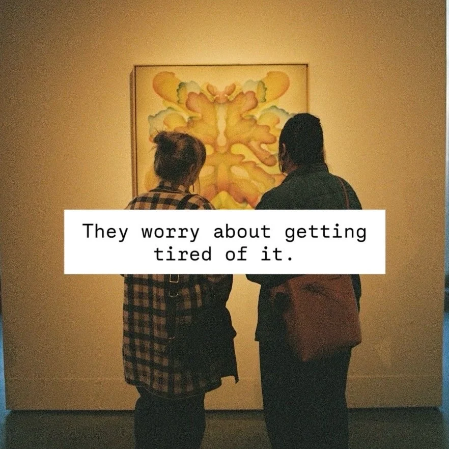 Two people, one wearing a checkered shirt and the other with a brown bag, stand in front of an abstract painting at an art gallery, looking at the artwork.