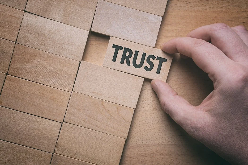 Hand selecting the word "Trust" out of a board of wooden blocks