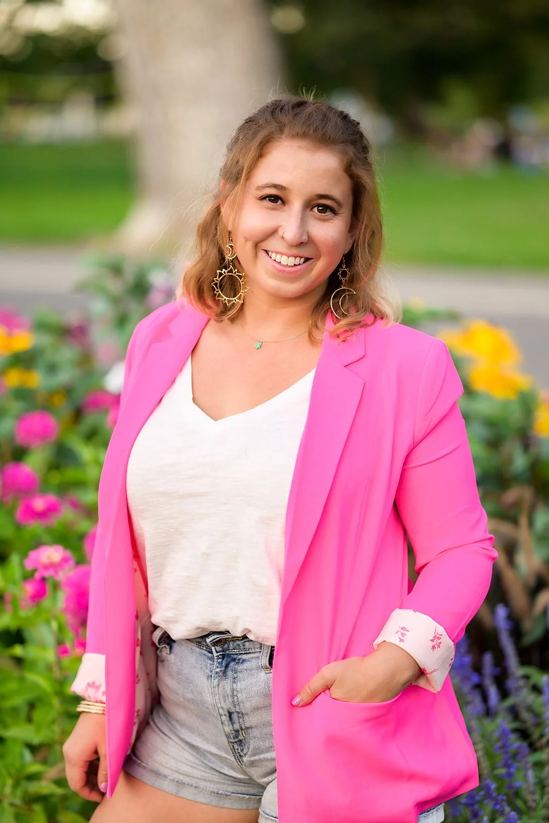 Sarah Fishman wearing a white shirt, pink blazer standing in front of pink and yellow flowers