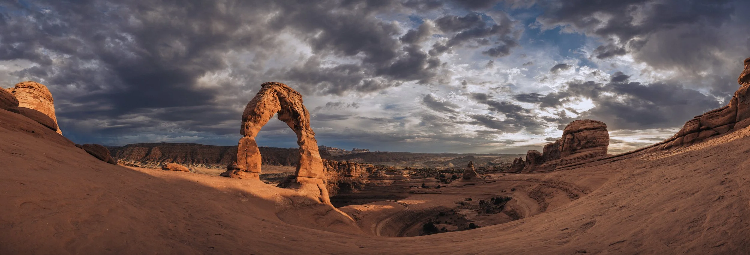 Delicate Arch in Arches National Park under cloudy sky at sunset.