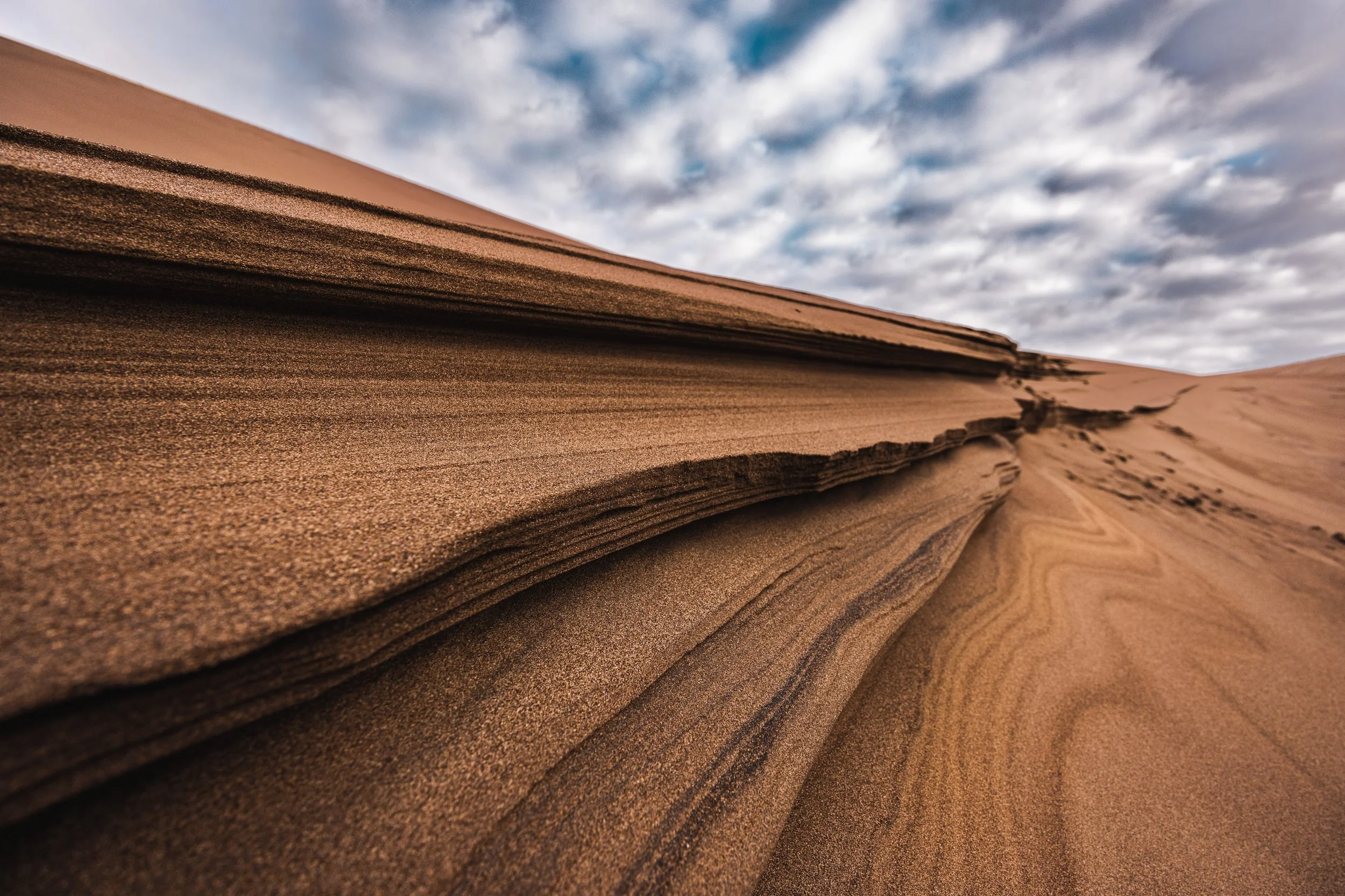 Close-up of layered sand formations in a desert with an overcast sky.