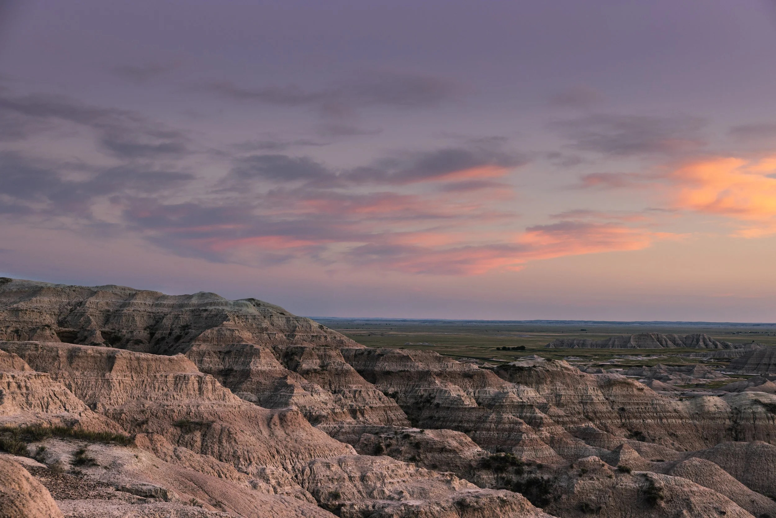 Sunset over Badlands National Park, showing rugged rock formations and colorful clouds.