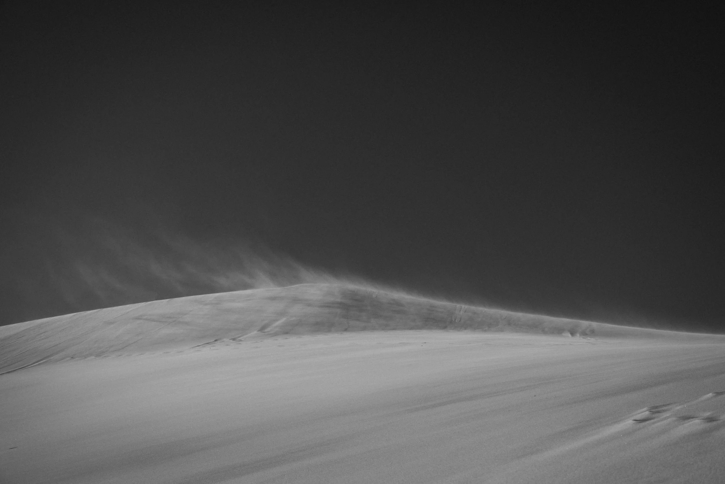 Black and white photo of a wind-blown sand dune under a clear sky.