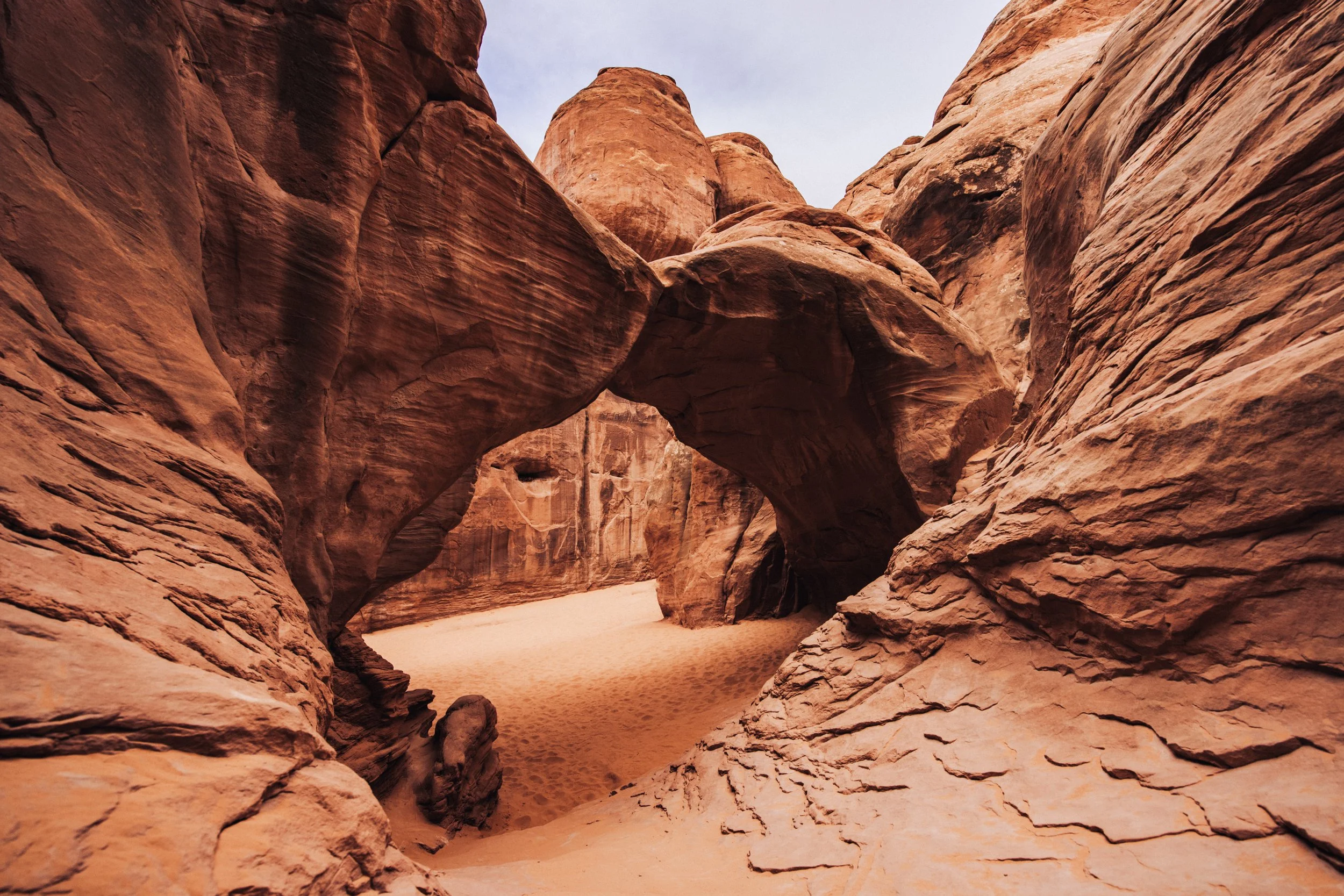 Natural rock arch in a red sandstone canyon, with a sandy path beneath it.