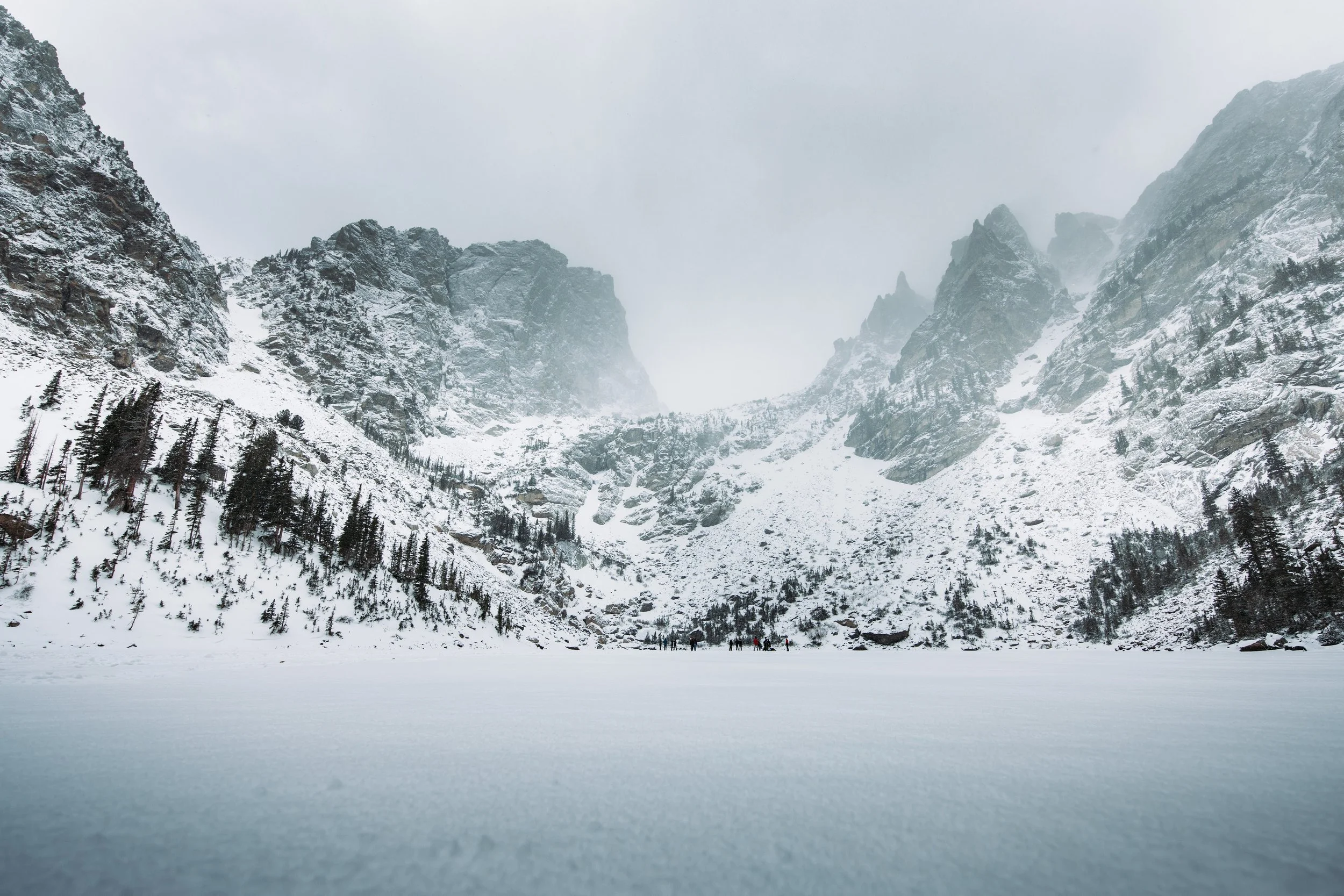 Snow-covered mountain landscape with pine trees and a cloudy sky.