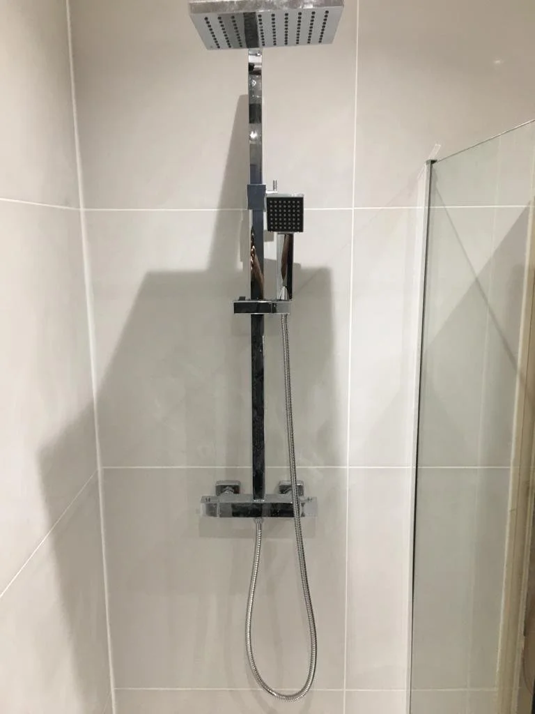 Modern shower with a large square overhead showerhead and a separate handheld shower attached to a vertical chrome bar, installed on a tiled wall.