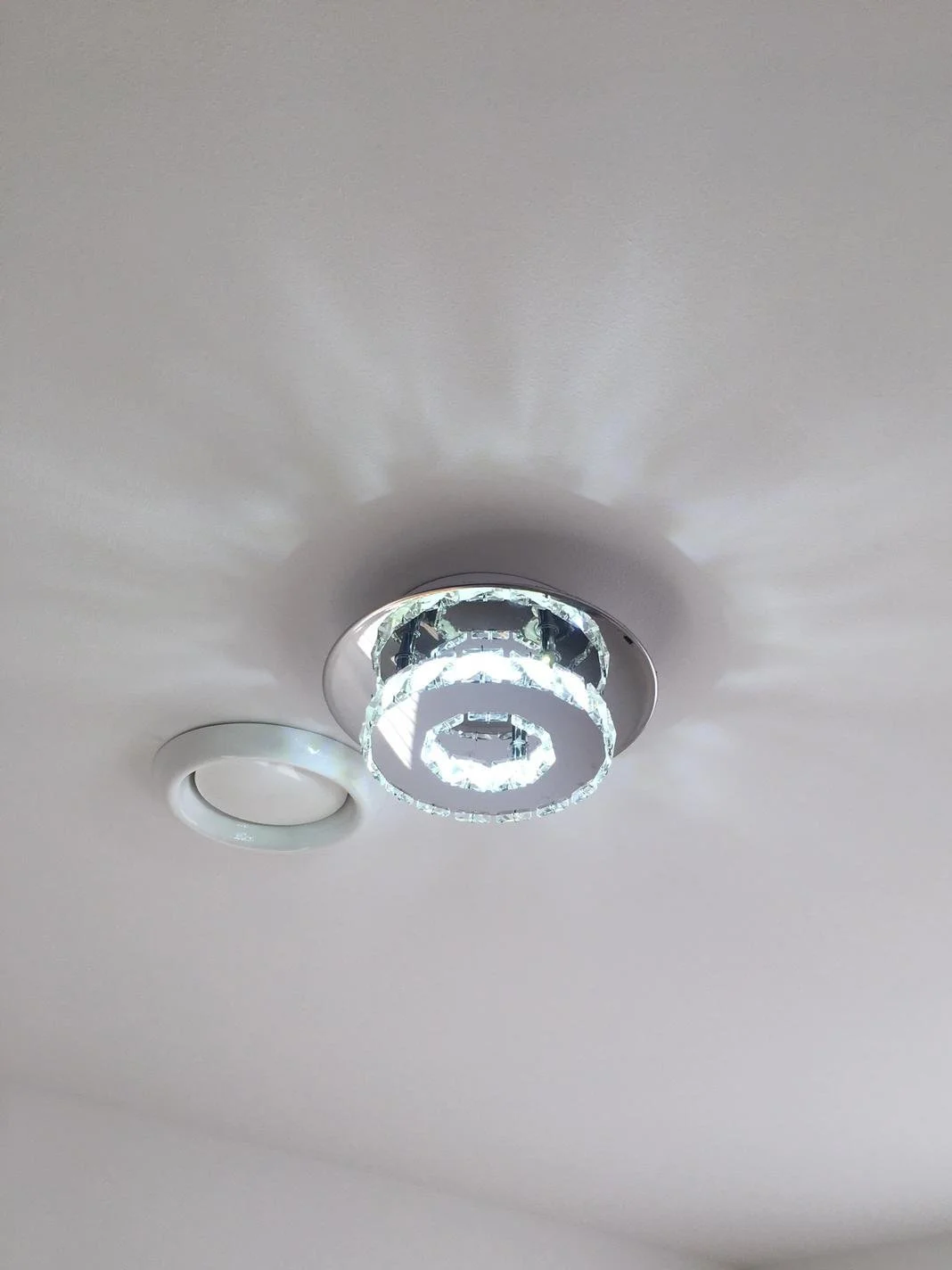 Ceiling light fixture with a modern, circular design emitting light and shadows on the ceiling.