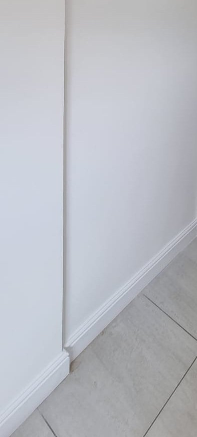 A corner of a room with white walls, a white baseboard, and light-colored tiled flooring.