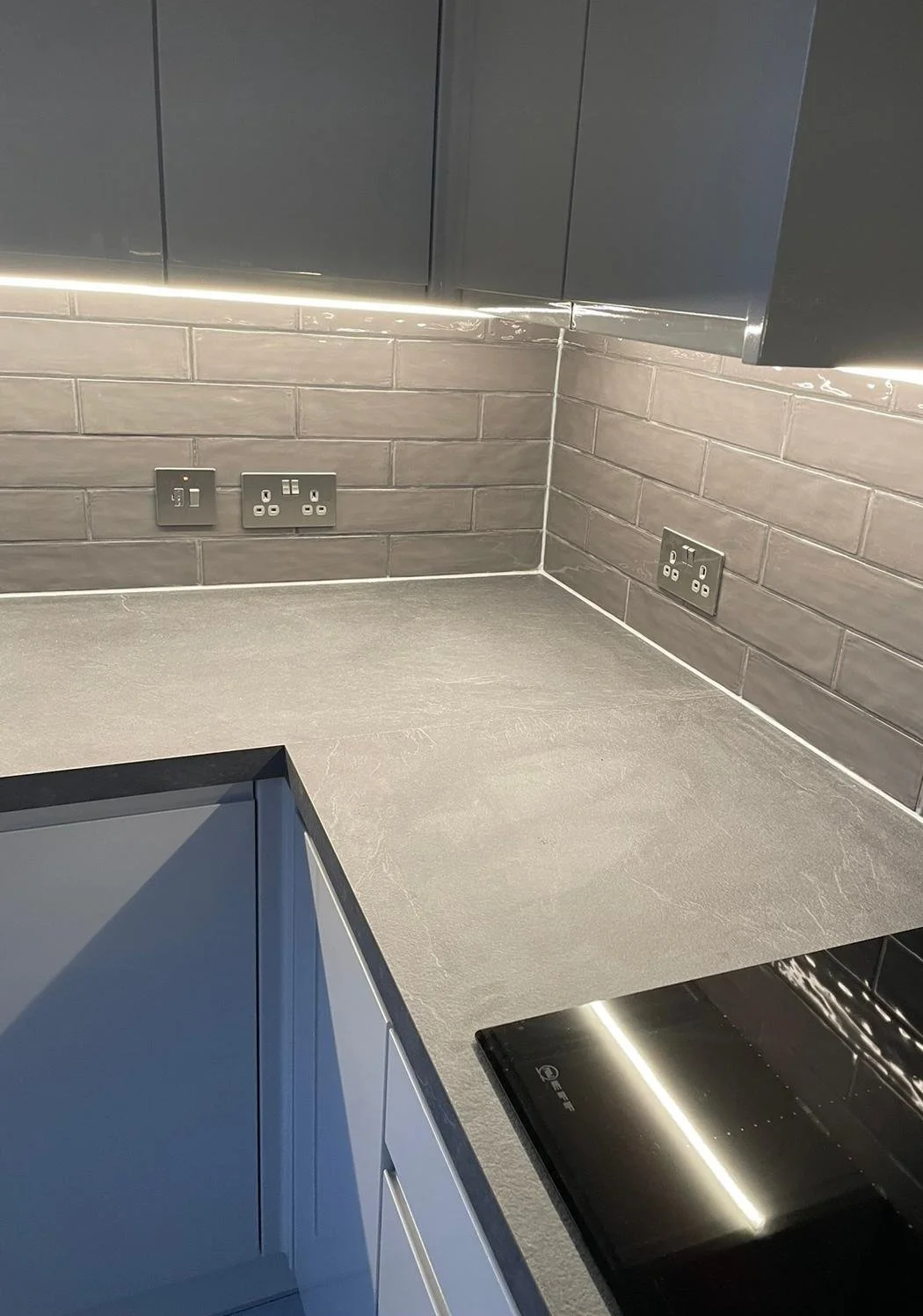 Close-up of a modern kitchen countertop with electrical outlets and a black stovetop.