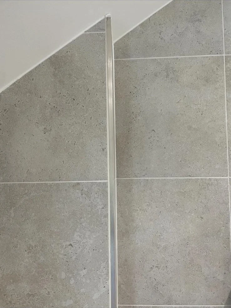 Close-up view of a metal strip on a tiled wall, with an angular ceiling in the top left corner.