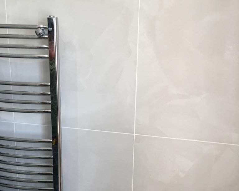 Close-up of a chrome towel rack mounted on a tiled bathroom wall.