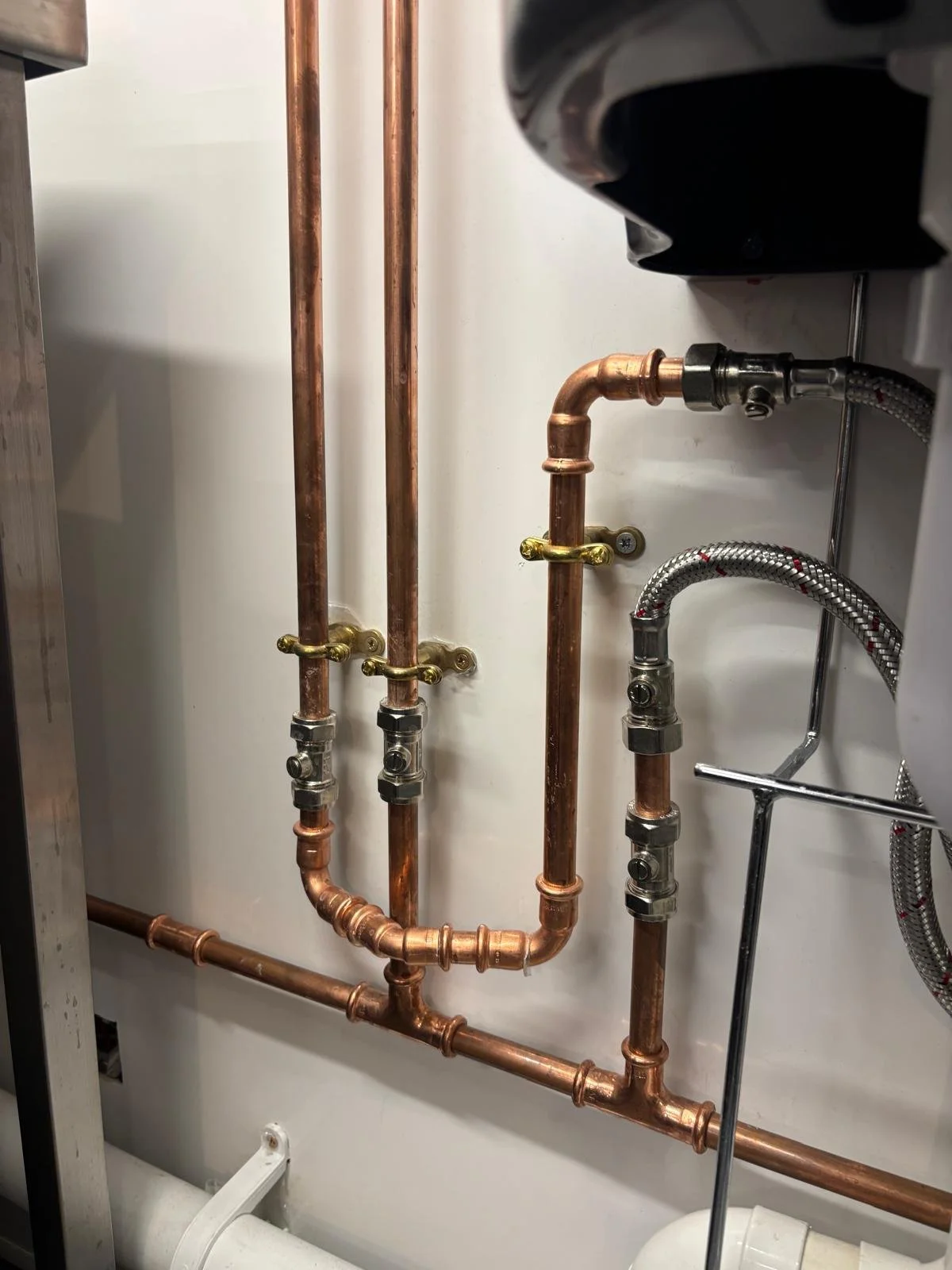 Close-up view of copper and flexible metal pipes with valves and fittings in a plumbing system.