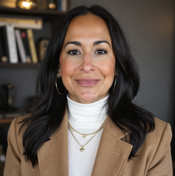 Professional woman with shoulder-length dark hair and purple highlights, wearing a black blazer and smiling at the camera against a plain white background.