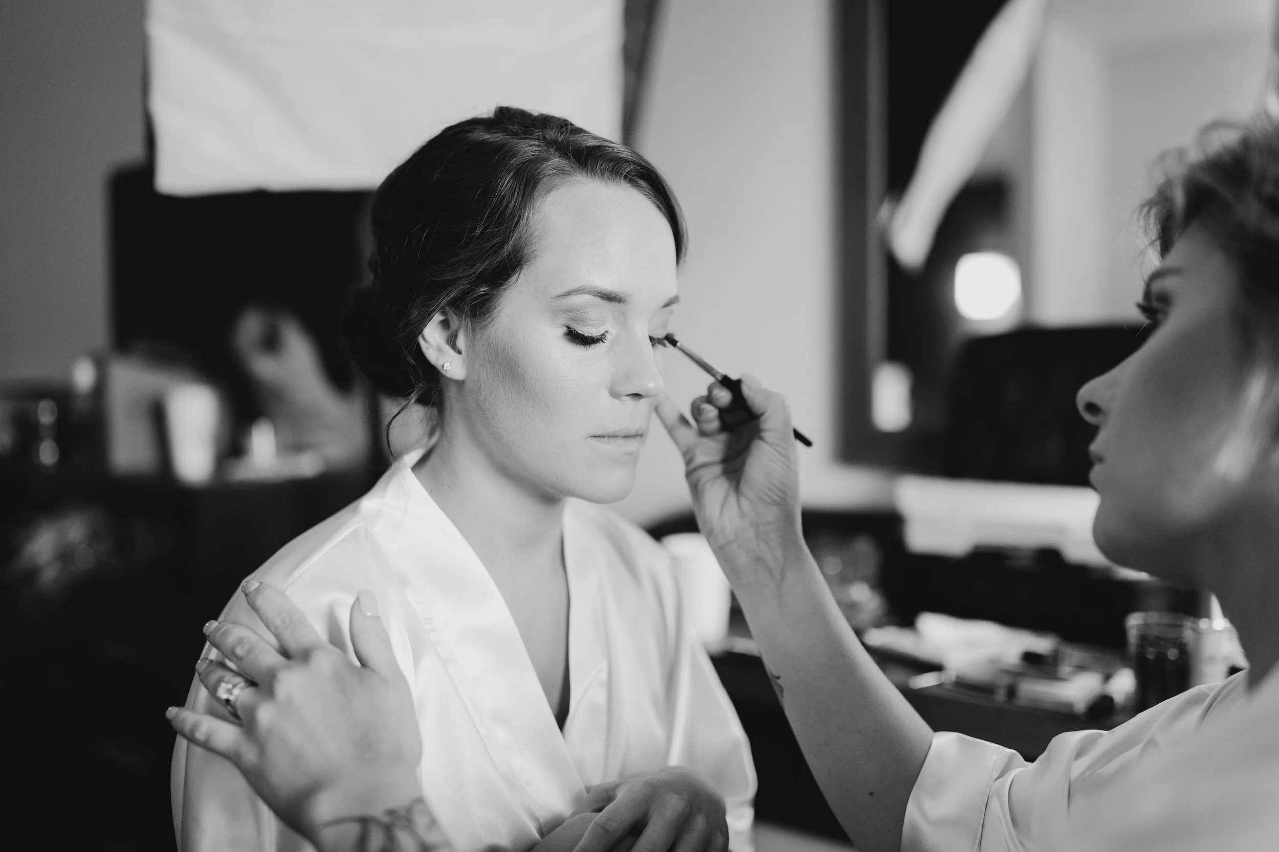 A woman with makeup being applied by a makeup artist in a professional setting.