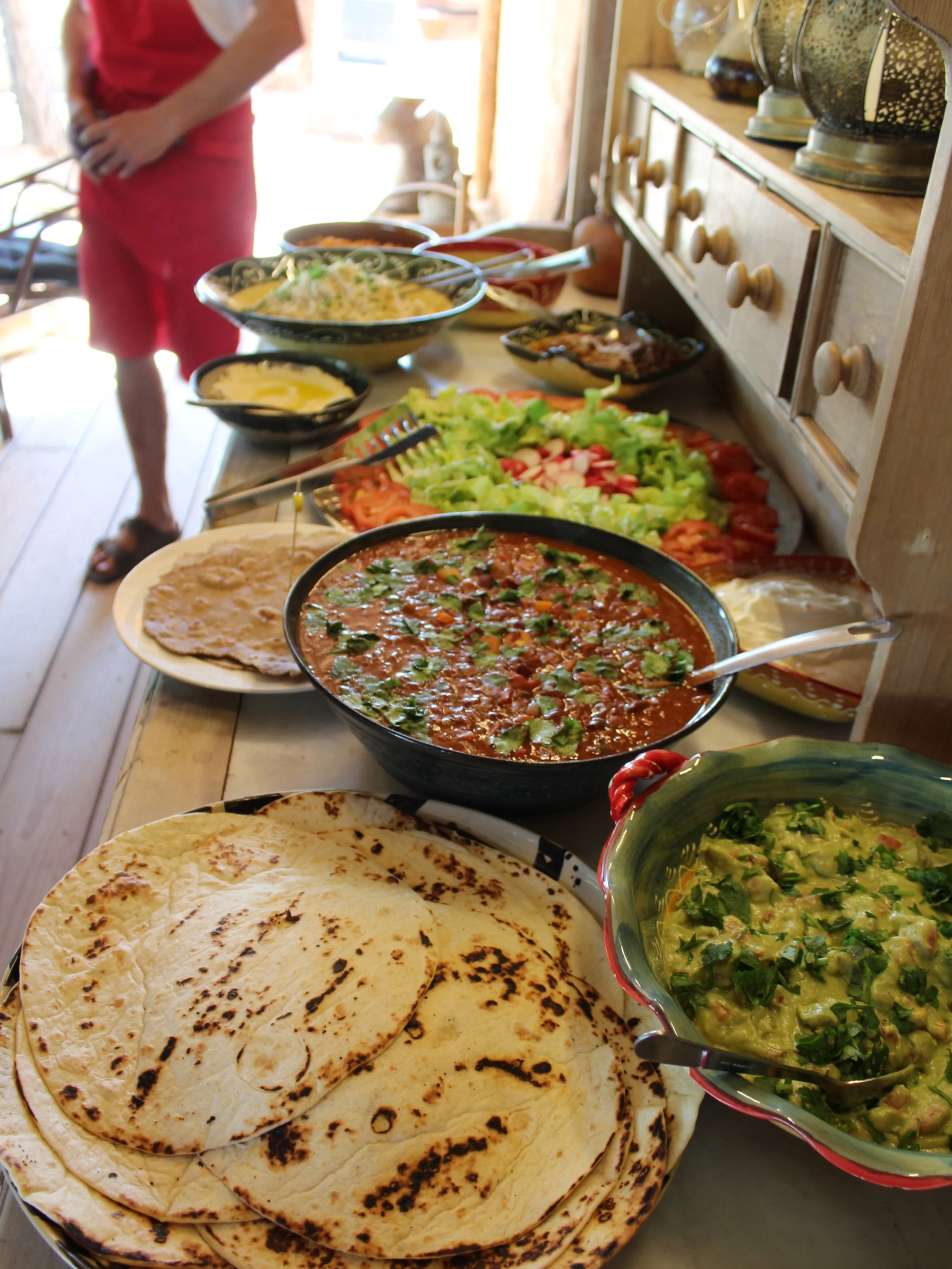 A spread of Mexican food including tortillas, salad, rice, beans, salsa, and various dishes on a wooden table.