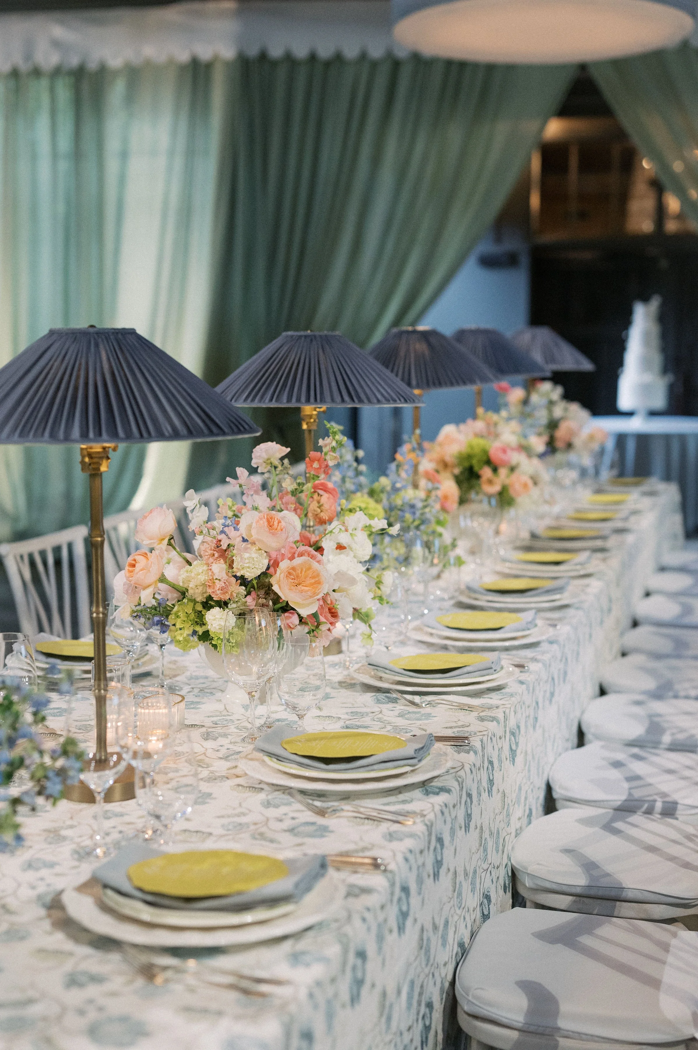 Elegant table setting with floral centerpieces, black lamps with gold accents, and neatly arranged plates and cutlery at a formal event.