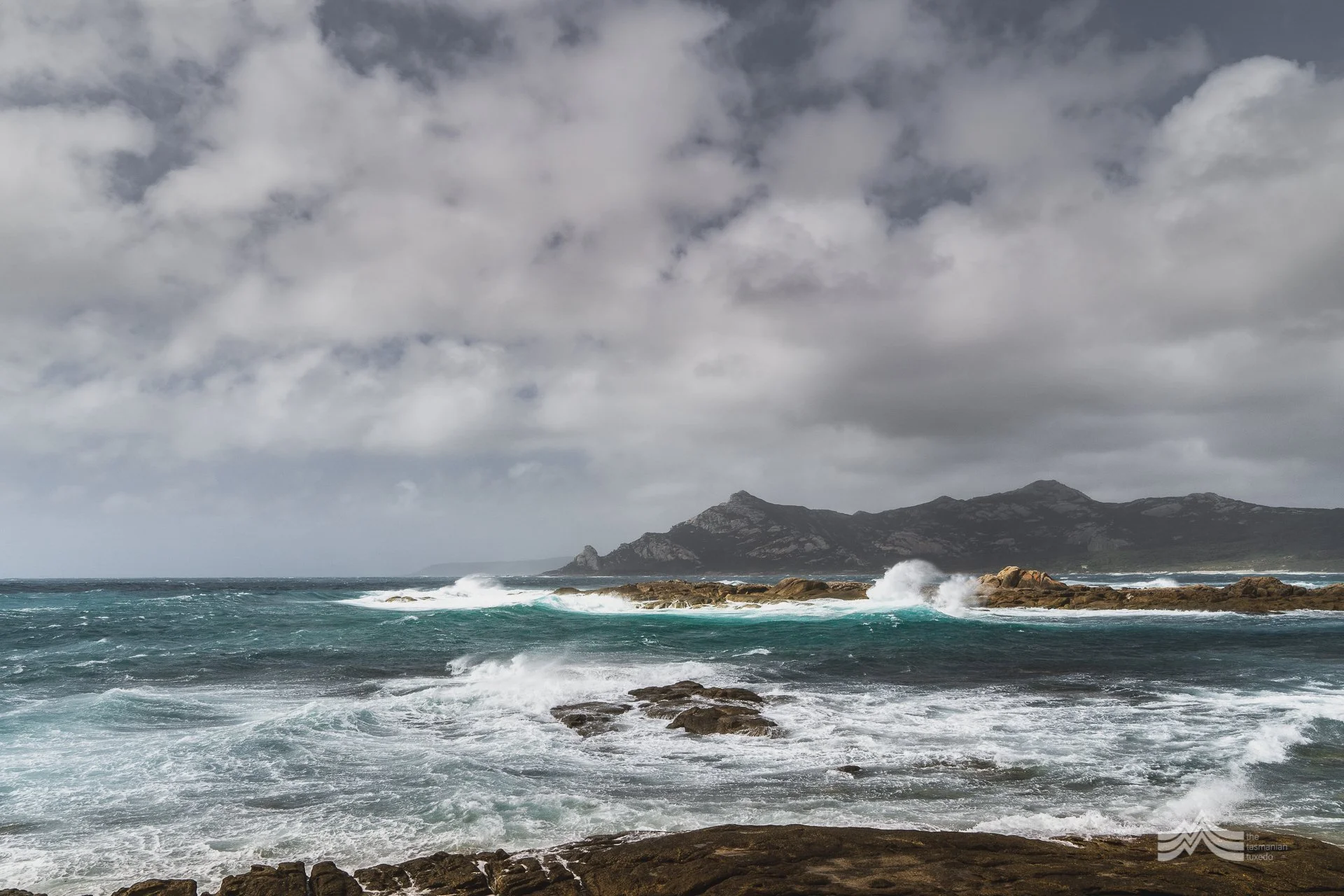 Ominous sky over a rugged coastline with waves crashing against rocks.