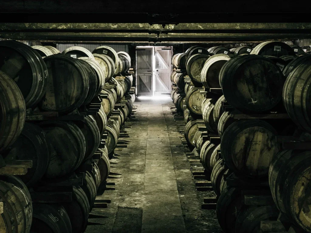 A cellar with oil barrels stacked in rows, leading to a doorway with light coming through.