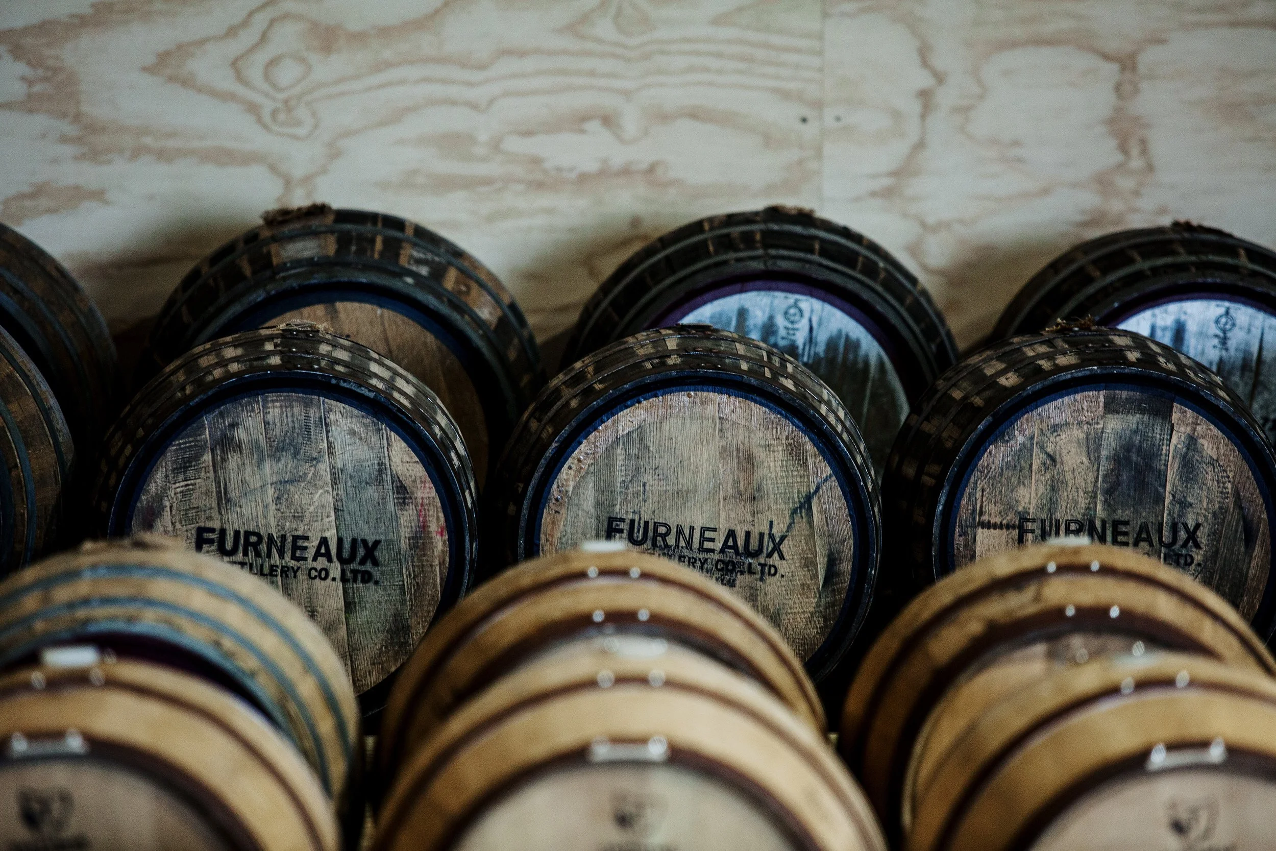 Stacked wooden barrels with metal bands, labeled 'FURNEAUX'. The barrels are arranged in a semi-circle with a textured stone or marble wall in the background.