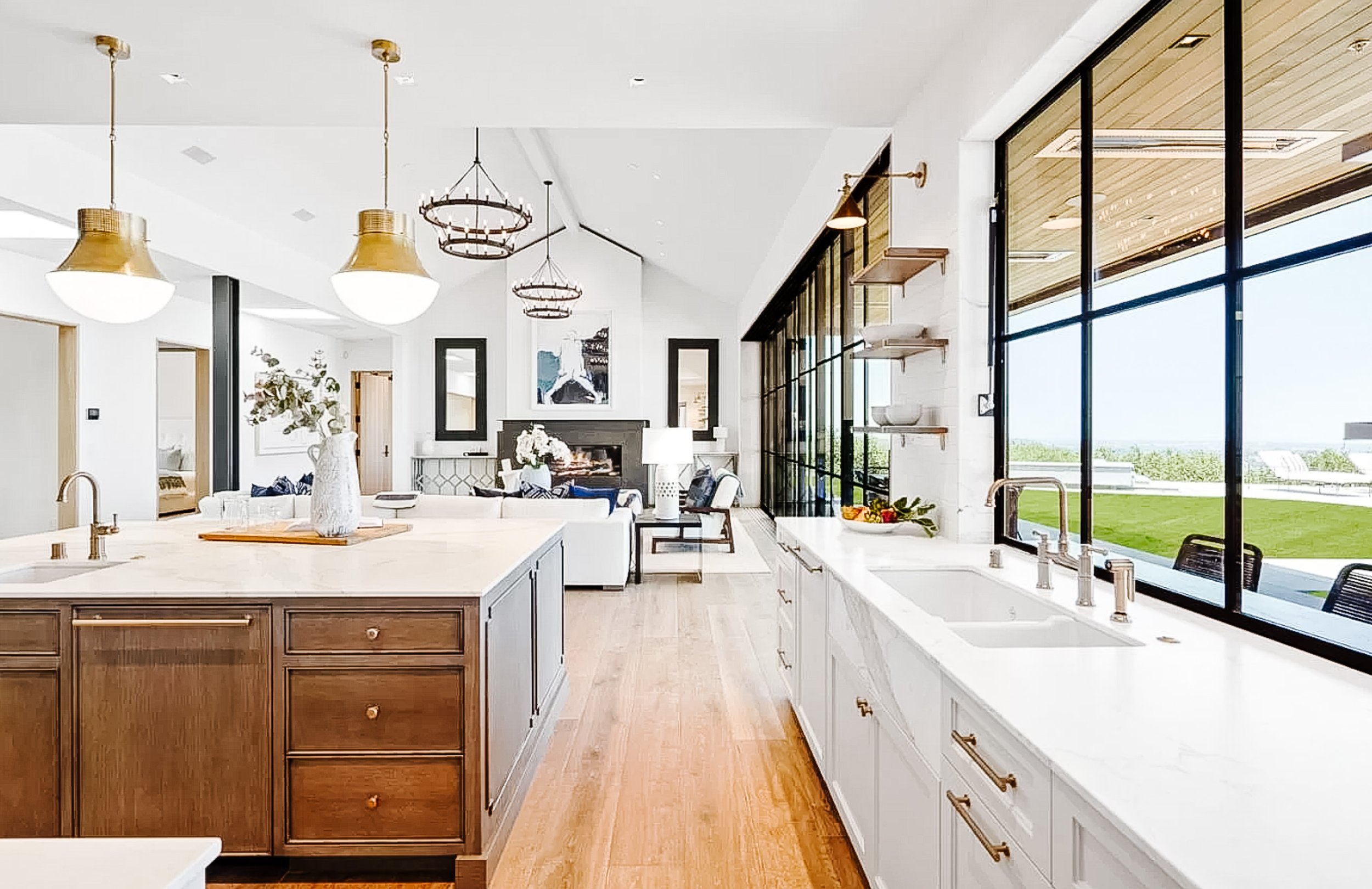Stunning kitchen has white perimeter cabinetry and contrasting island, all with Calacatta marble countertops, full-height backsplashes, and brushed gold hardware and fixtures; separate breakfast room with woven light fixture and double French doors t