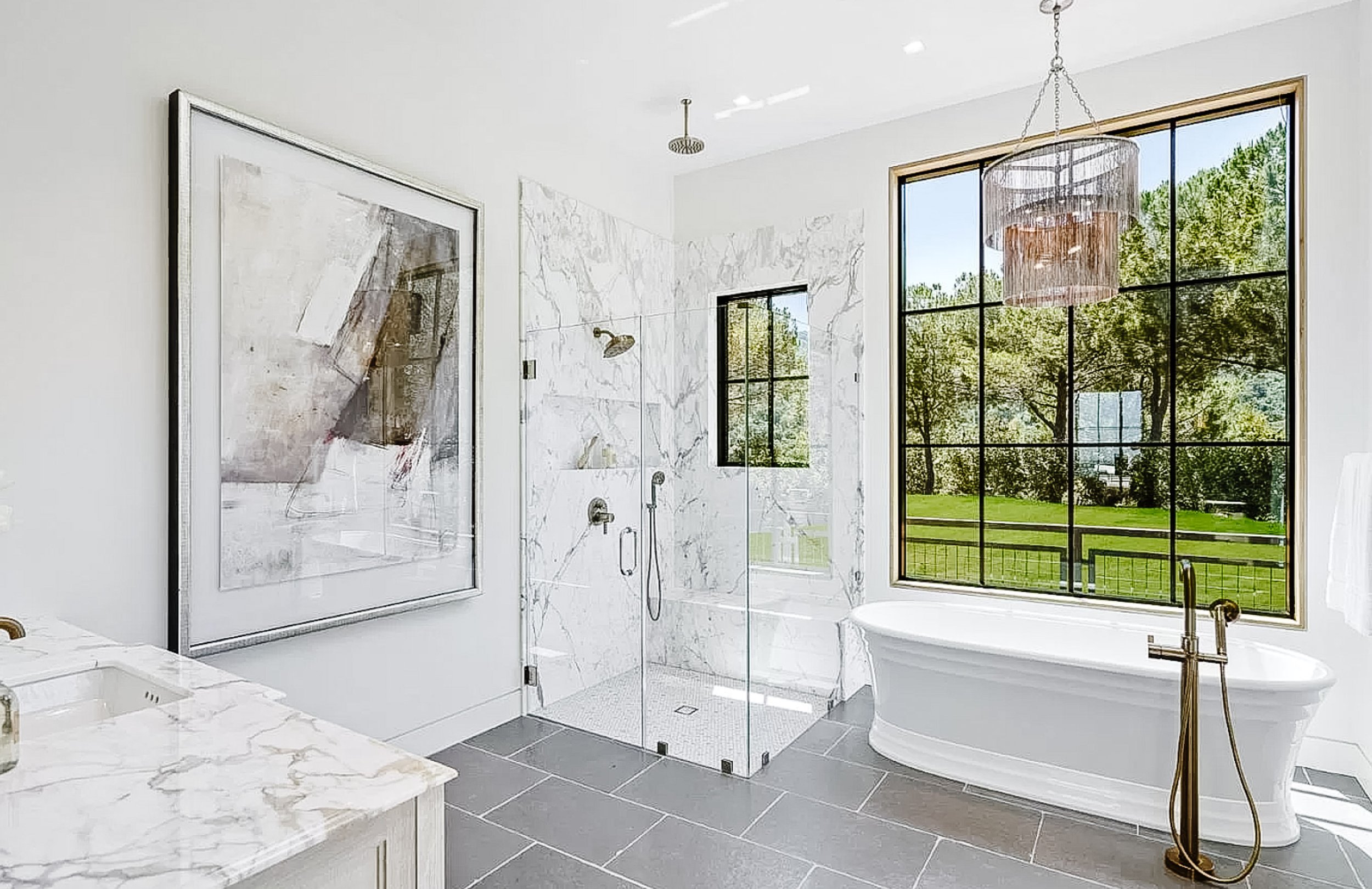 Curbless shower with book-matched marble walls, free-standing tub, private automated commode room, and sliding glass doors to an outdoor shower