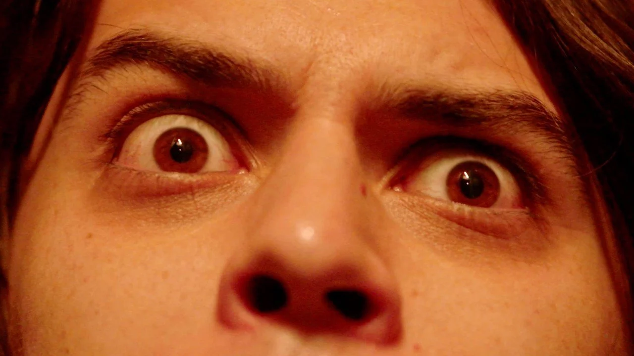 Close-up of a person's face with wide-open eyes and an upward gaze.