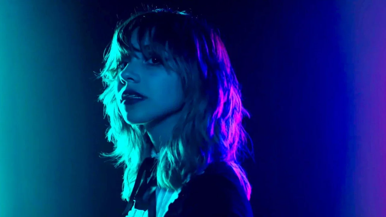 A woman with wavy hair illuminated by blue and purple neon lighting.
