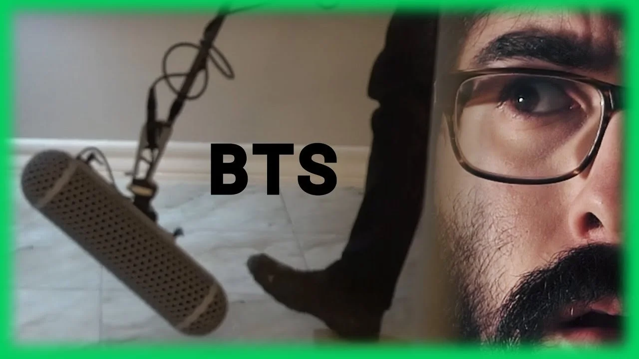 Close-up of a man's face with glasses, a beard, and mustache, with a microphone and a person's foot in the background, the word 'BTS' in the center, and a green border.