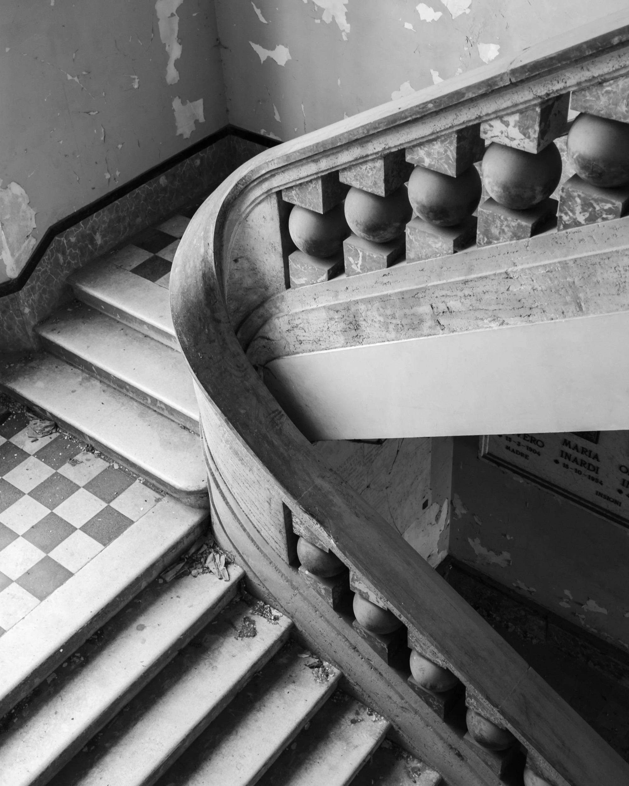 A curving stone staircase over a checkerboard floor, in black and white