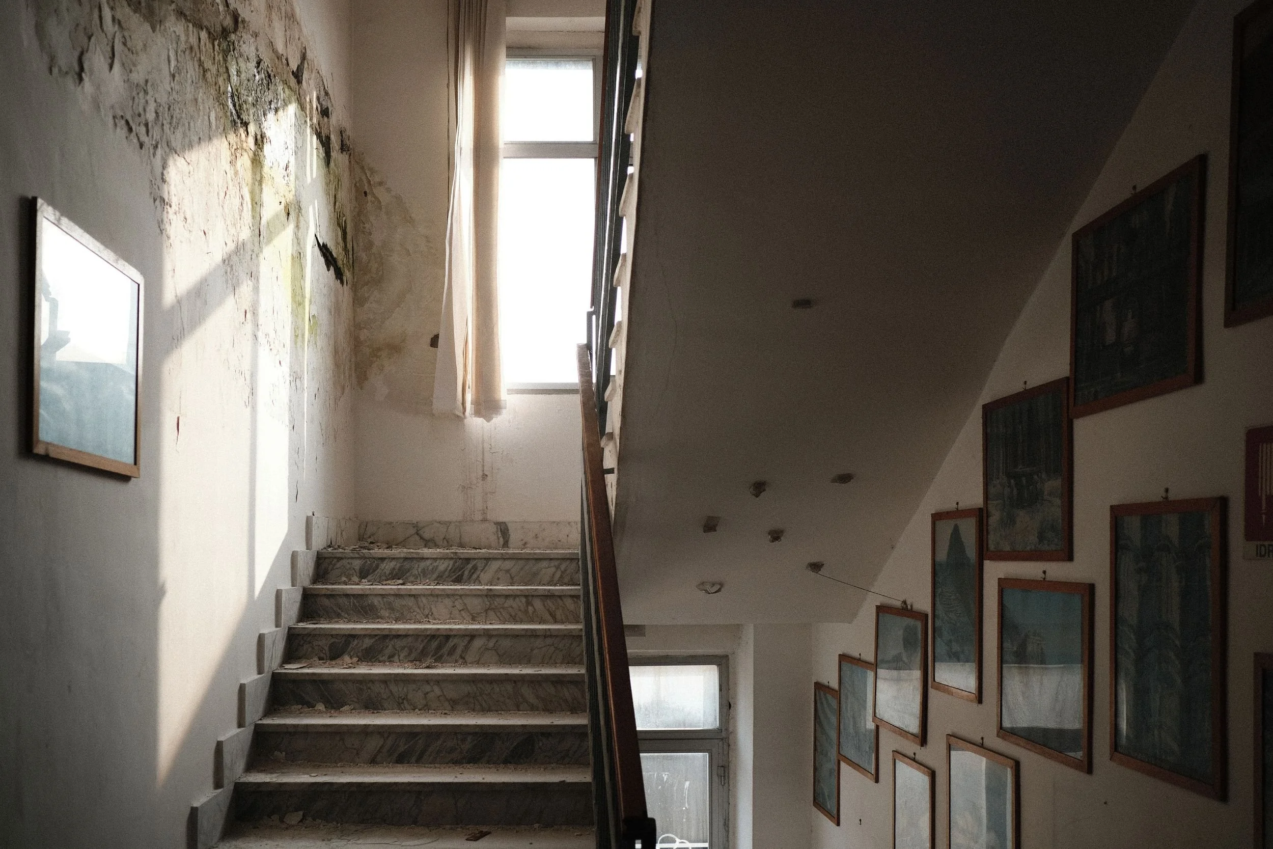 A staircase with picture frames on the walls, light coming from a window